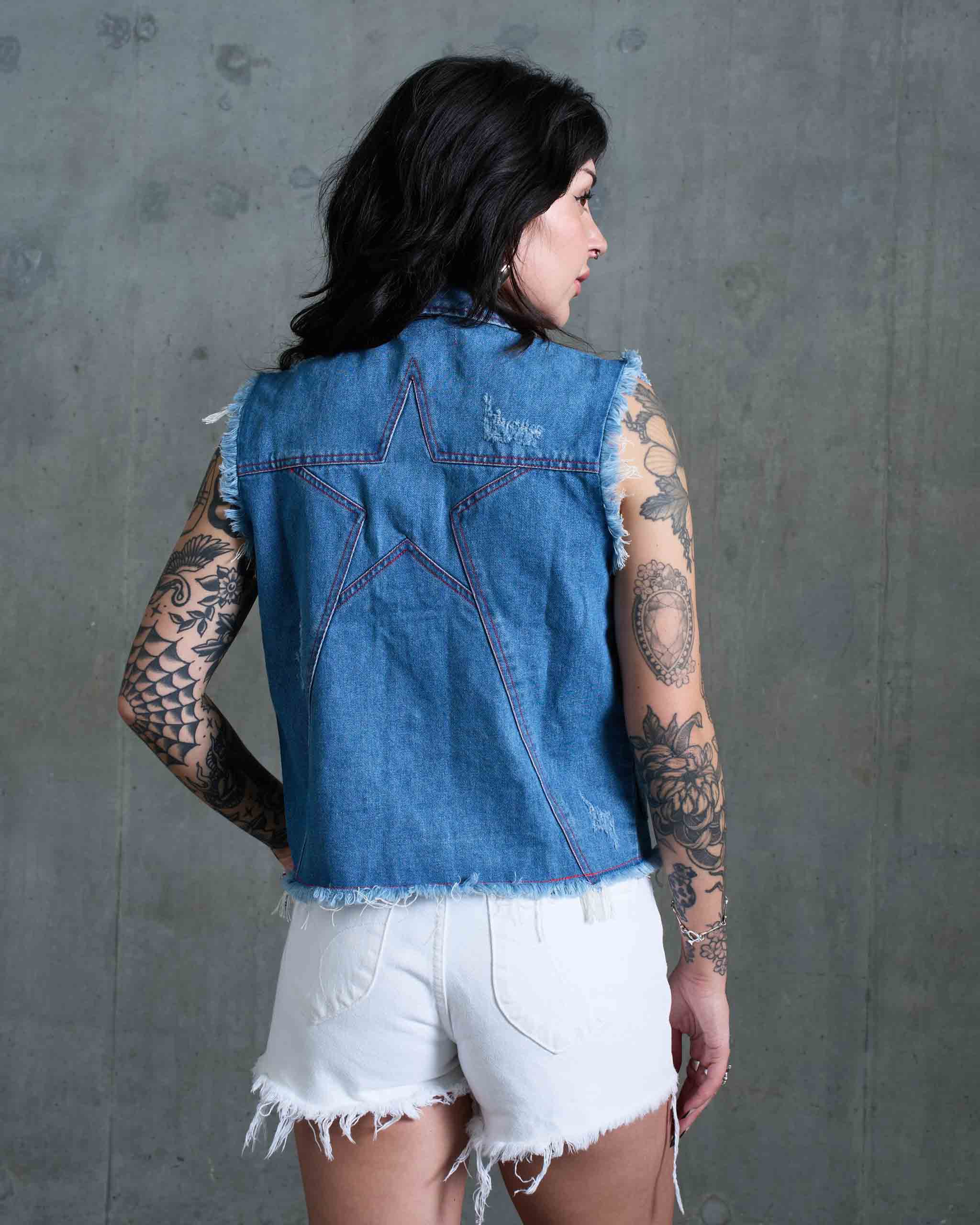 A tattooed model wearing a denim vest with a big star panel on the back.