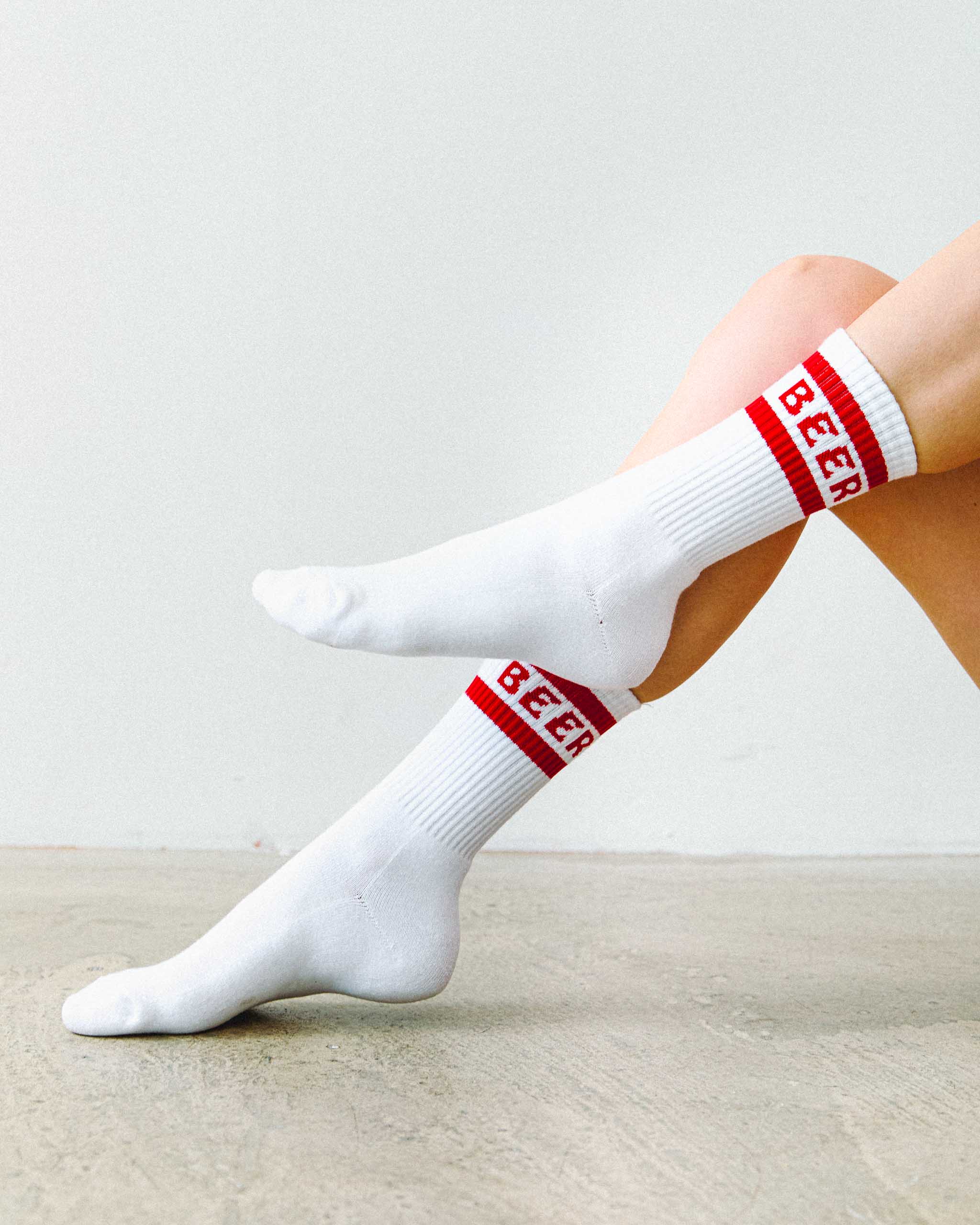 White cotton crew socks with red 'BEER' text worn by a person on a light background