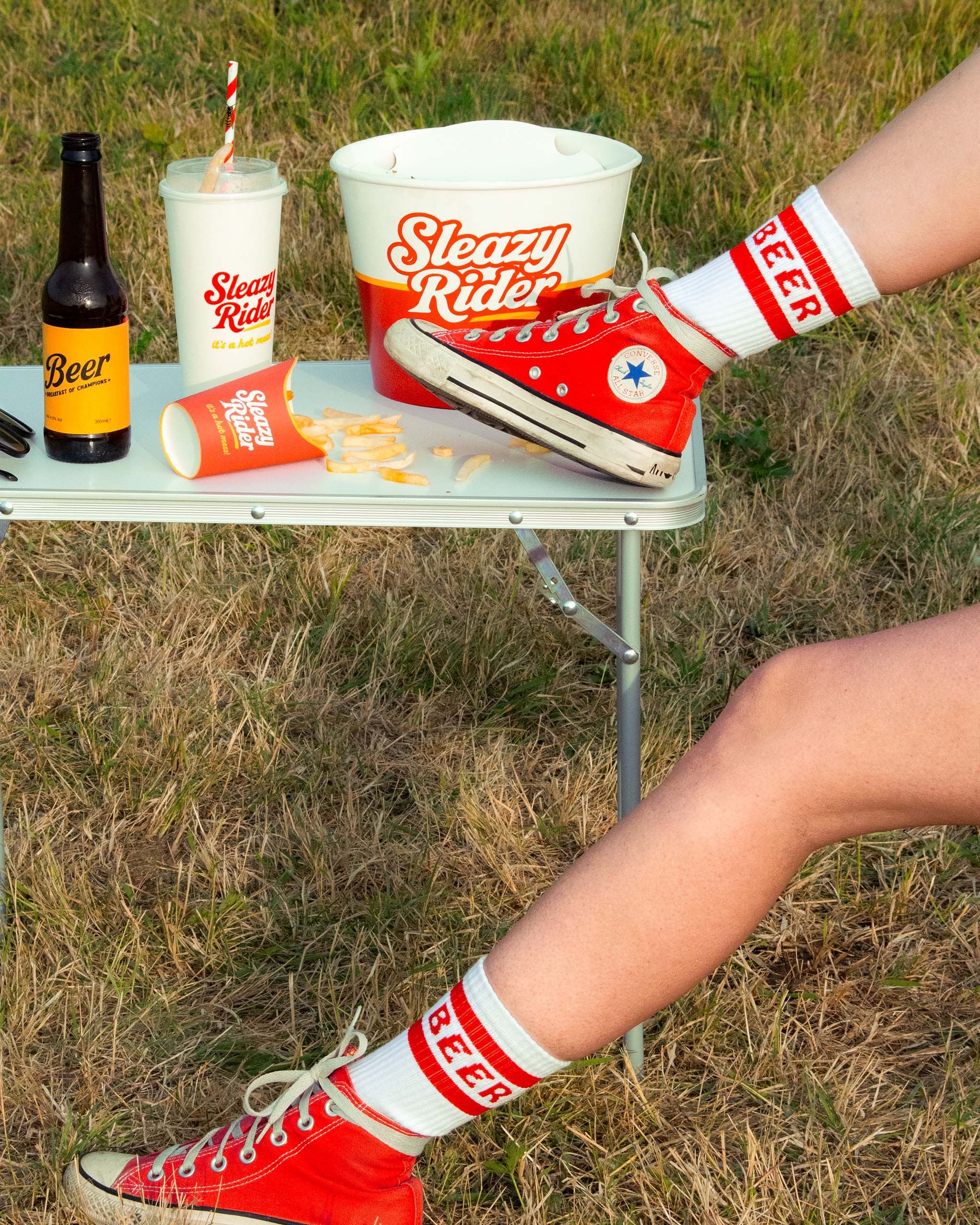 Person wearing red sneakers with Sleazy Rider "Beer" socks.