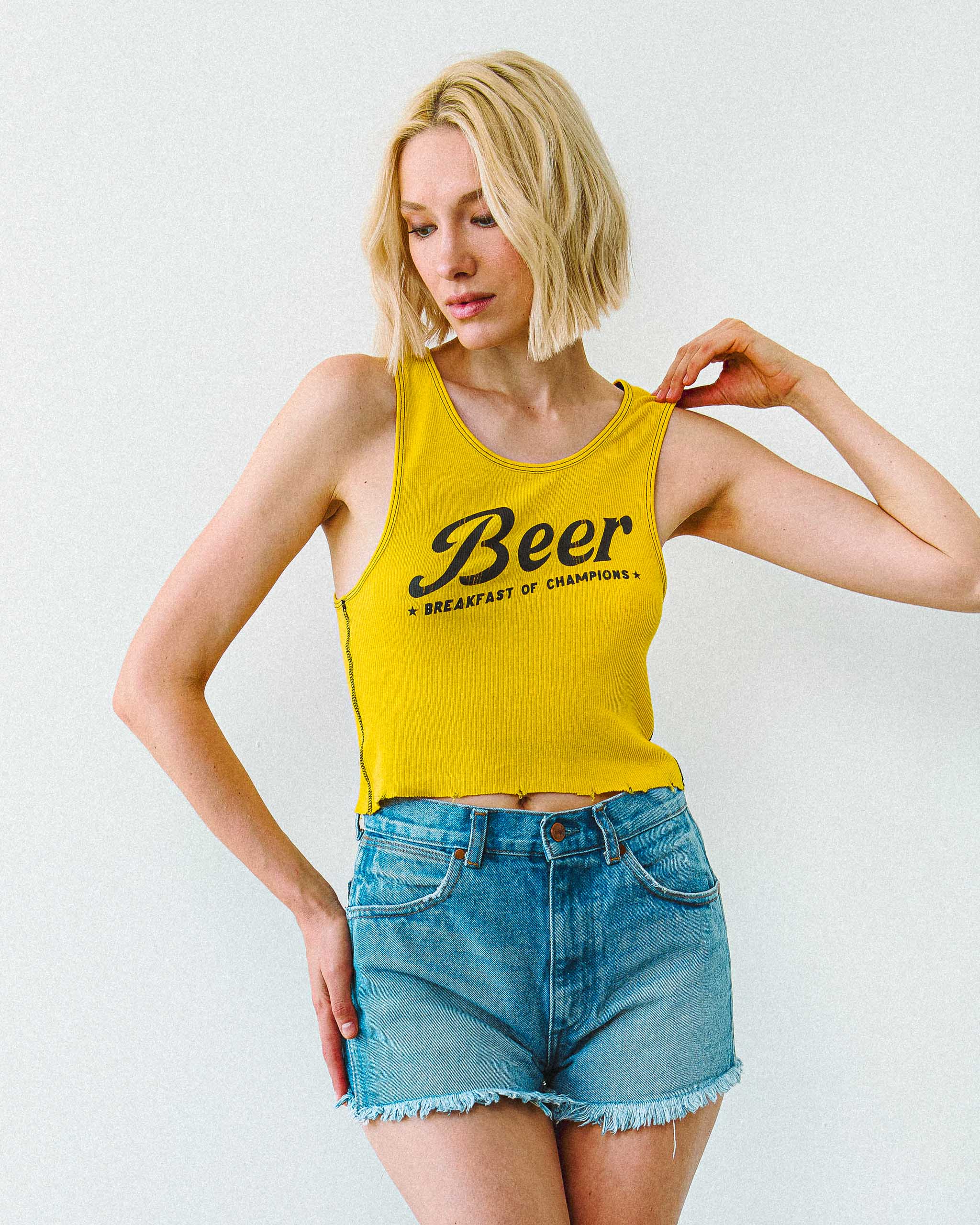 A woman wearing a yellow "Beer, Breakfast of Champions" tank top and denim shorts.