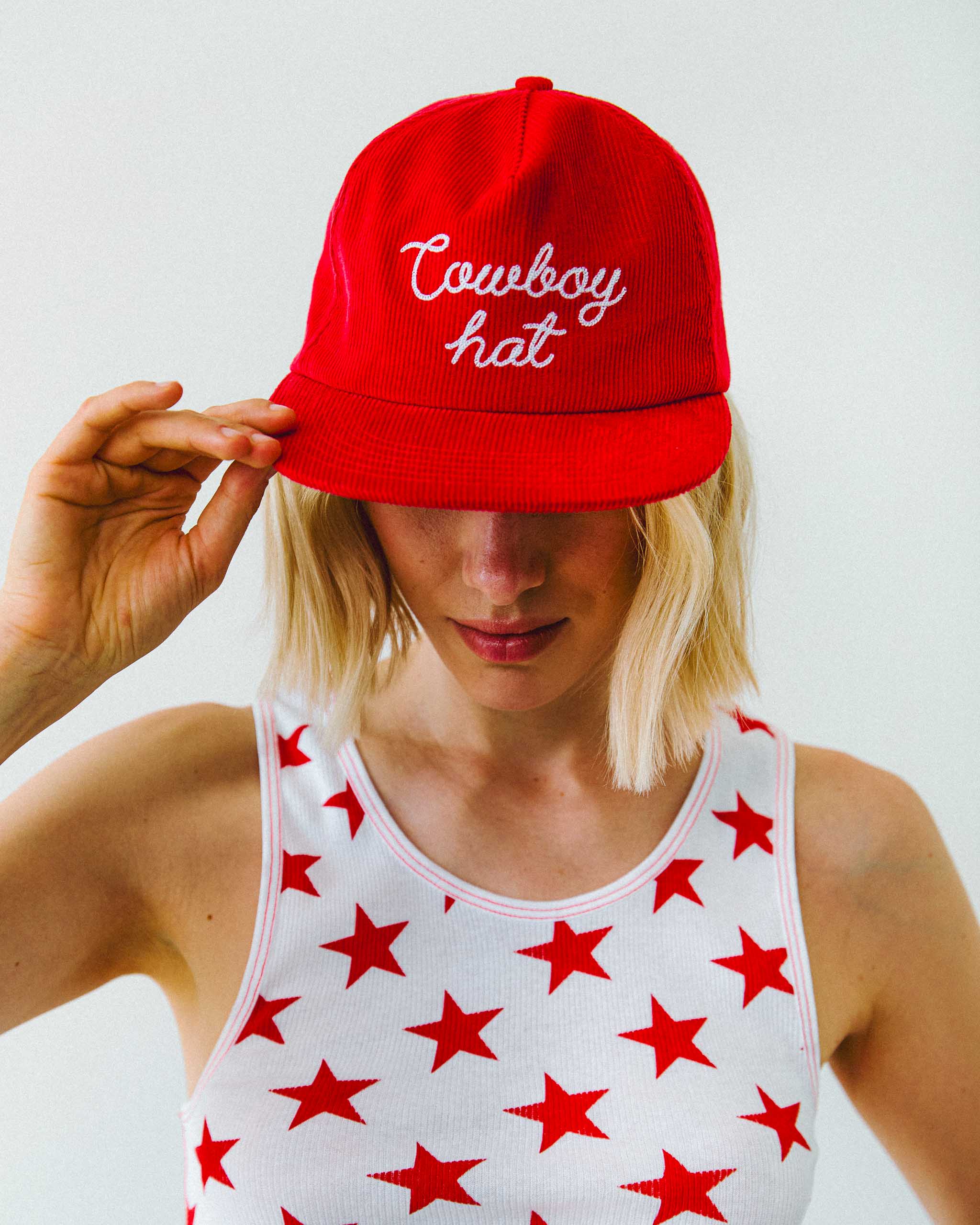 Person wearing a red cap with 'Cowboy hat' text and a star-patterned tank top against a plain background.