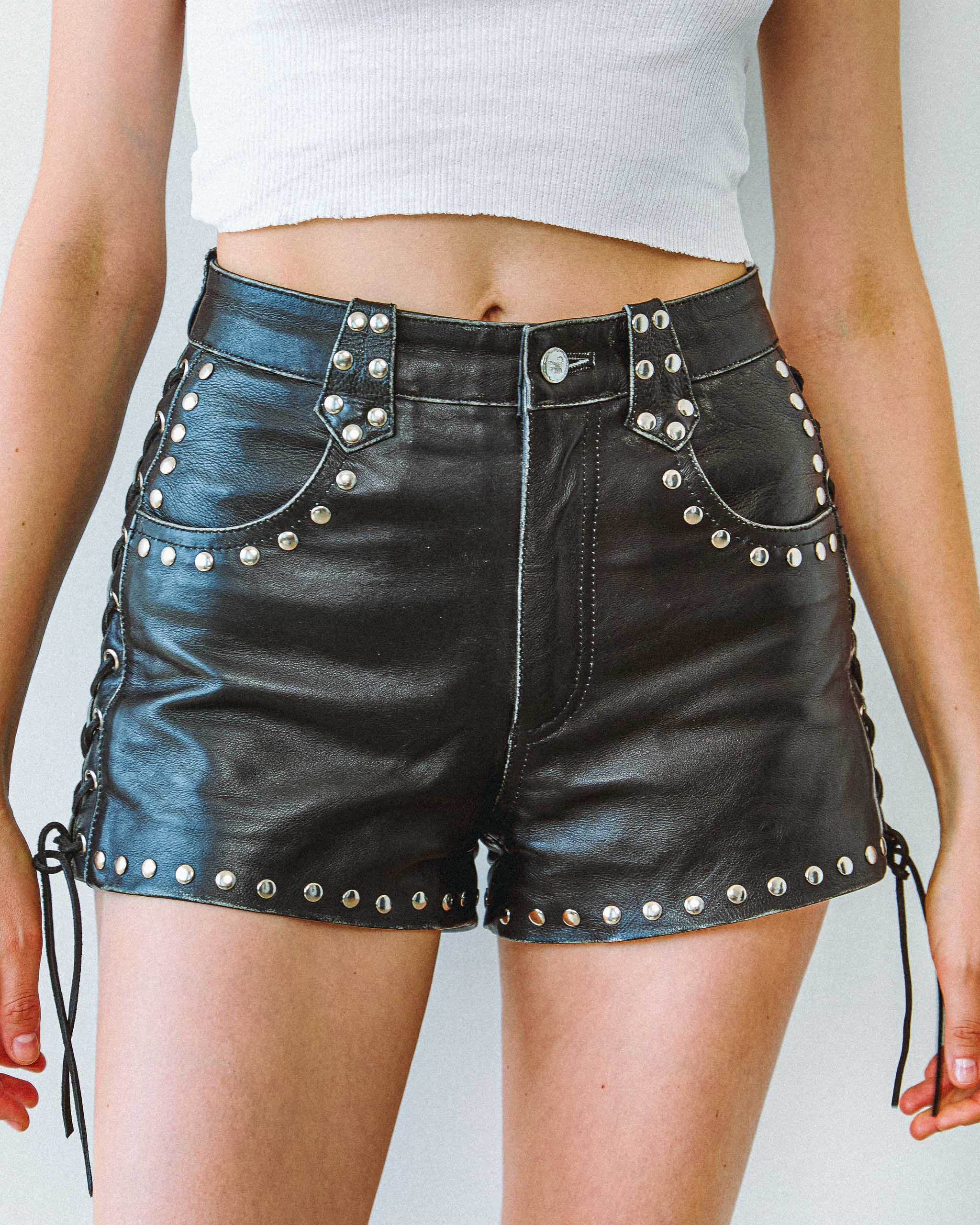 Sleazy Rider Coyote studded black leather shorts with silver studs worn by a person on a plain background. Biker and western vintage inspired style.