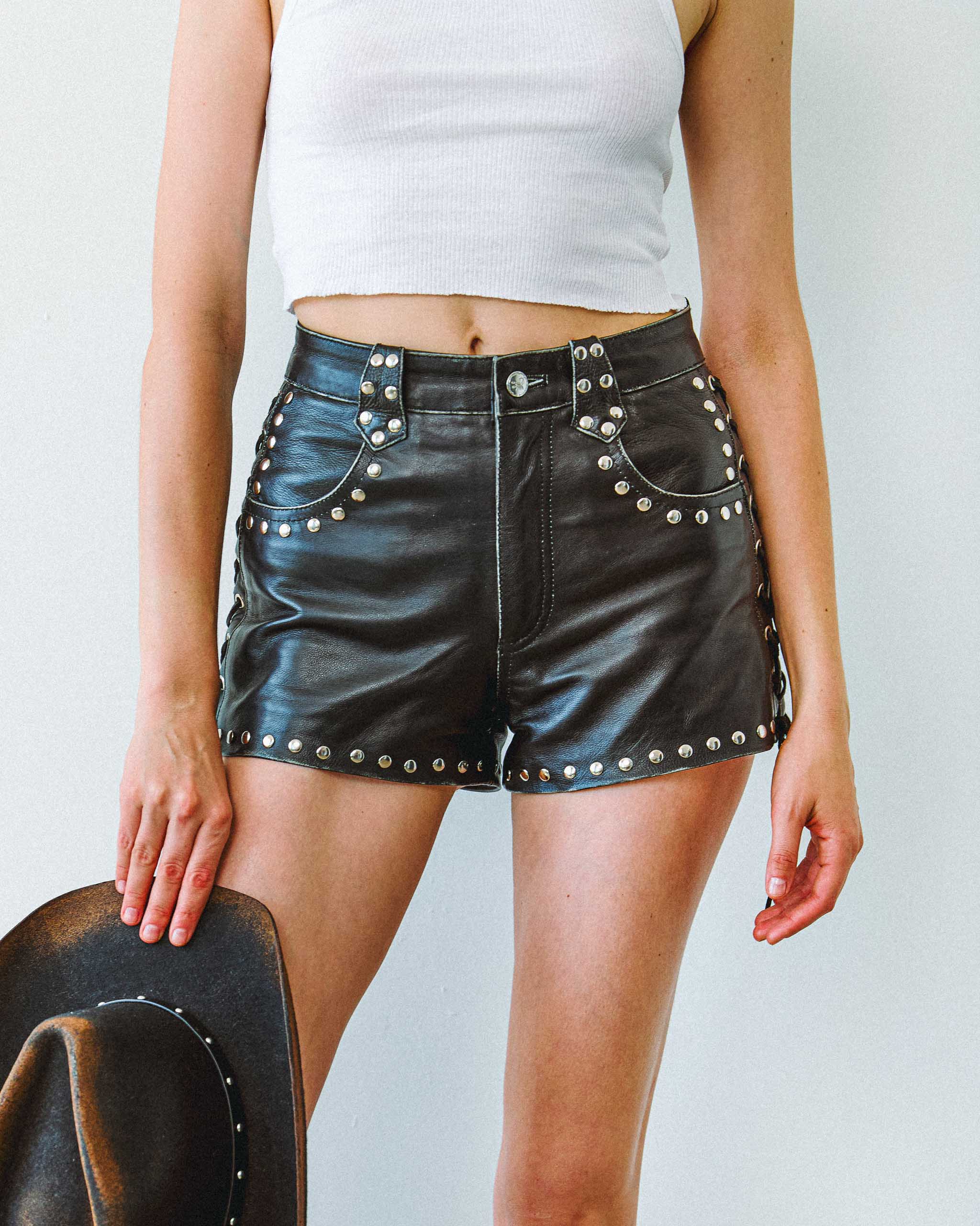 Model wearing black studded leather western shorts and cowboy hat.