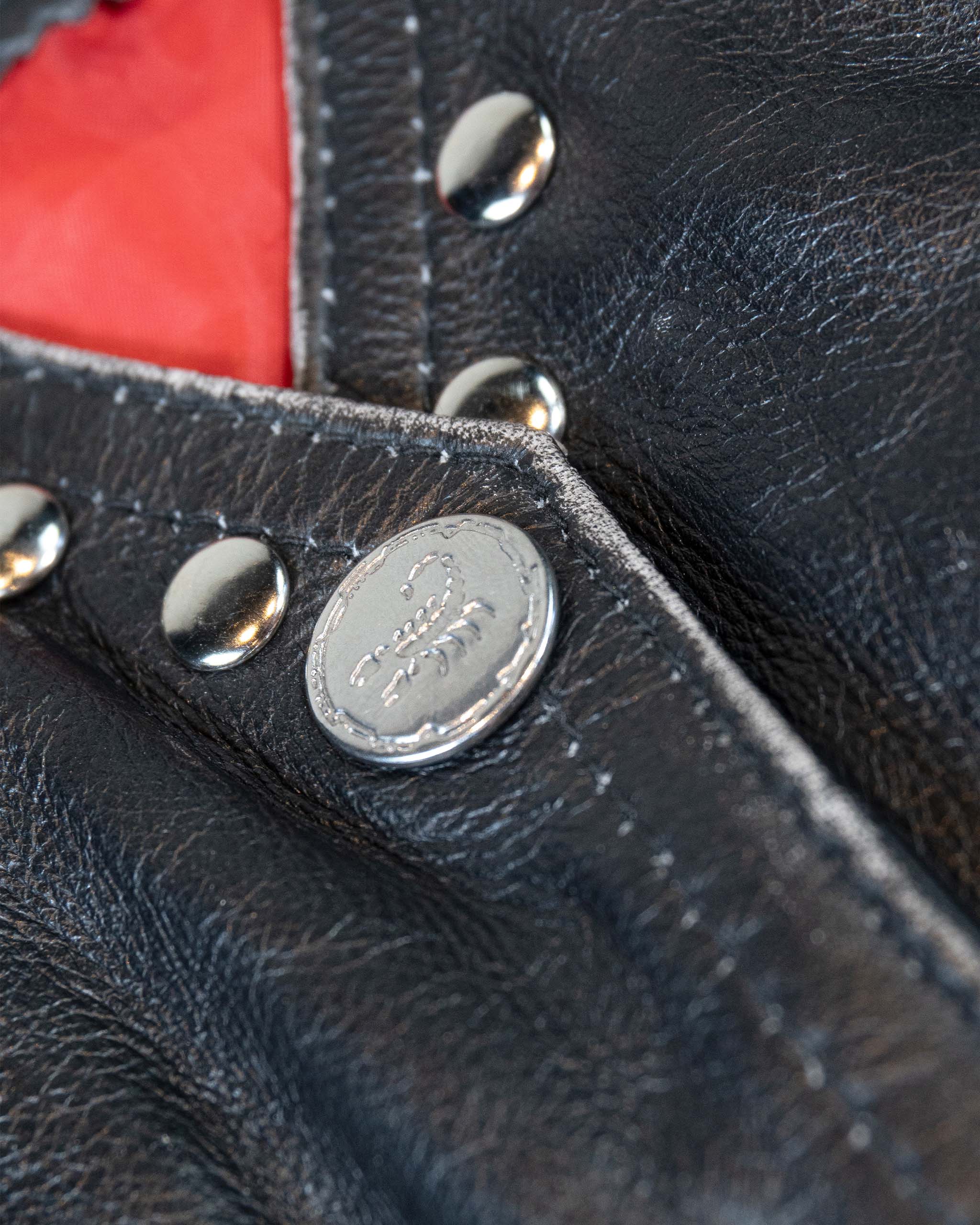 Close-up of a black studded leather vest with silver scorpion buttons and a red interior.