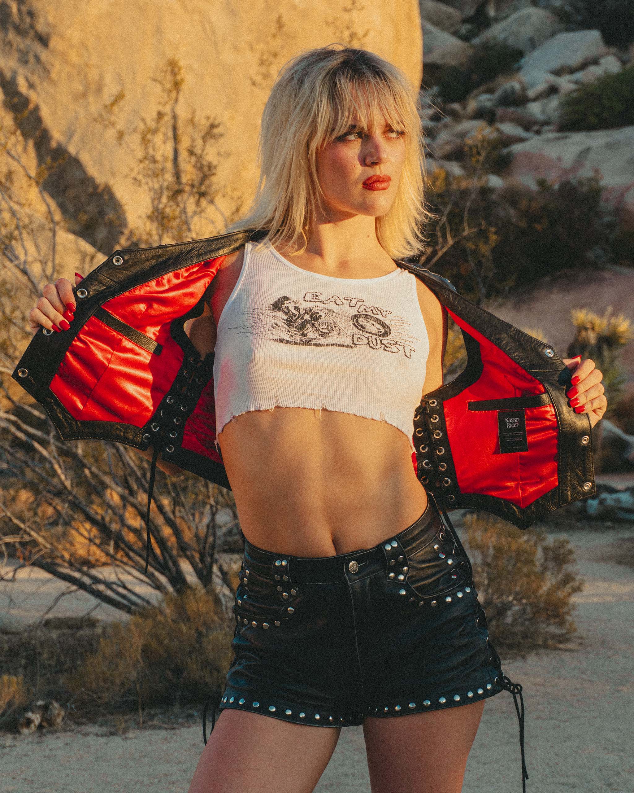 A model wearing the Sleazy Rider Coyote Studded Leather vest and shorts with satin red lining and lace up sides. Vintage biker style outfit with a desert backdrop.