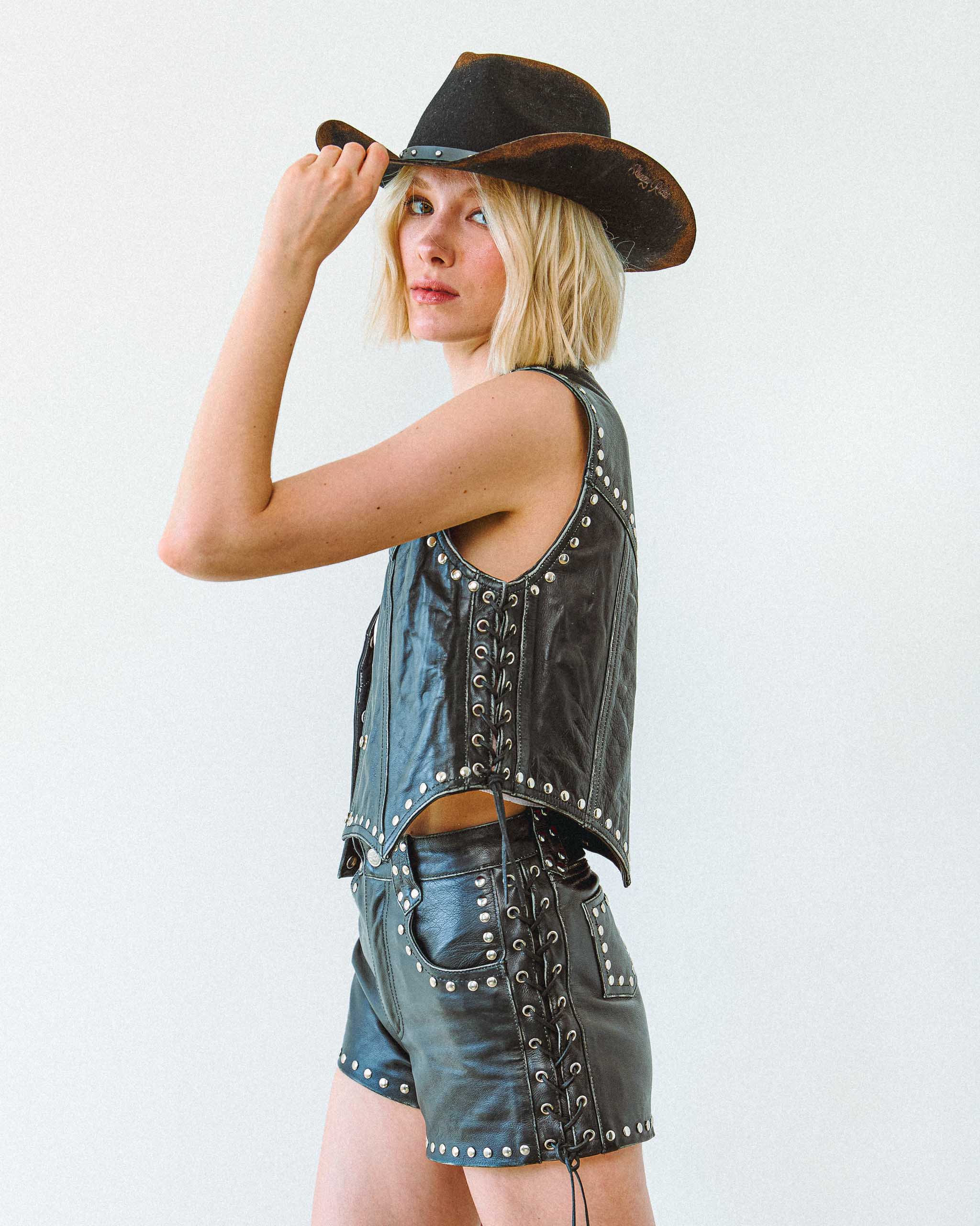 A young woman wearing the Sleazy Rider coyote studded leather vest and shorts, for bikers and cowgirls.