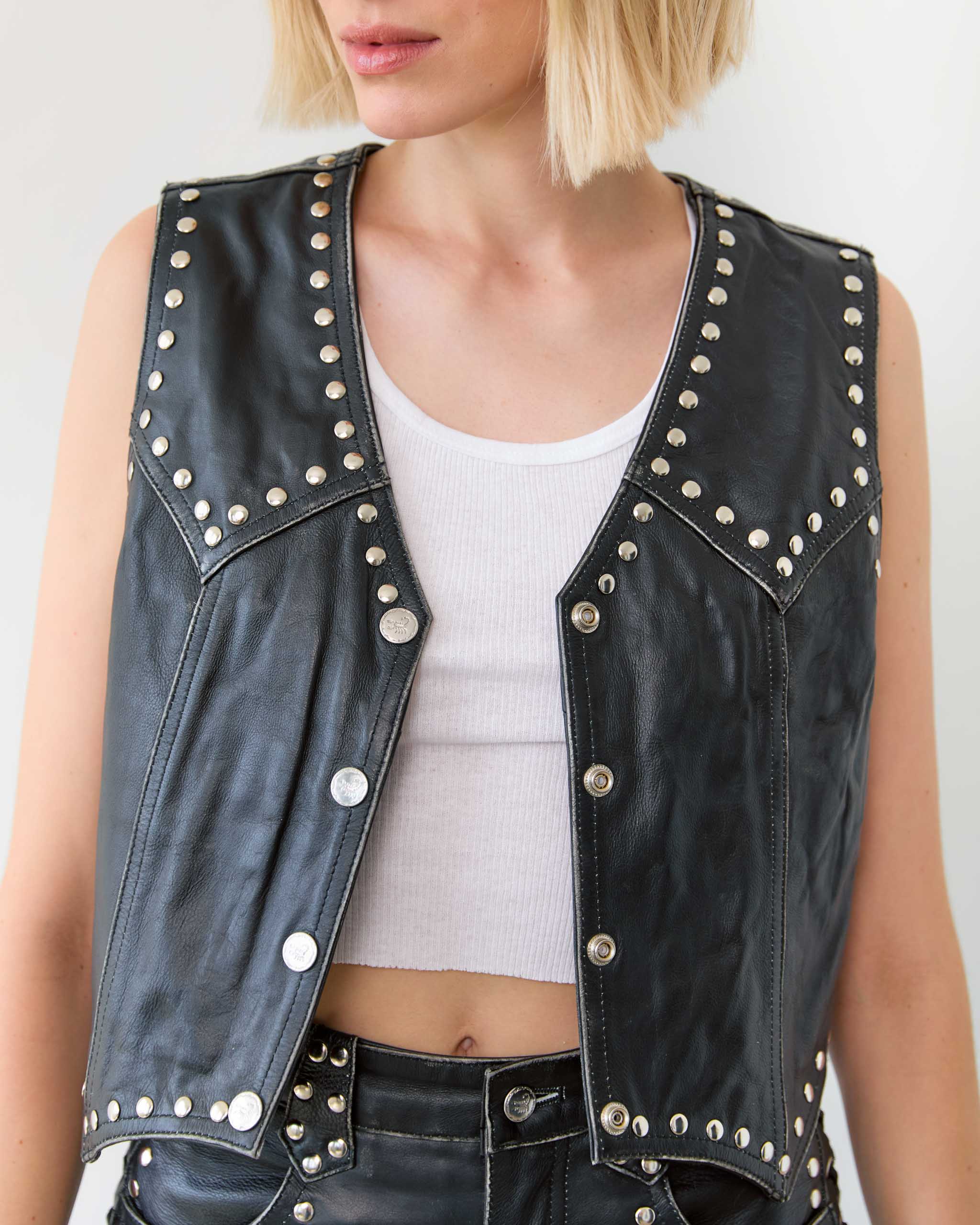 Black leather western vest with studs worn by a person on a white background