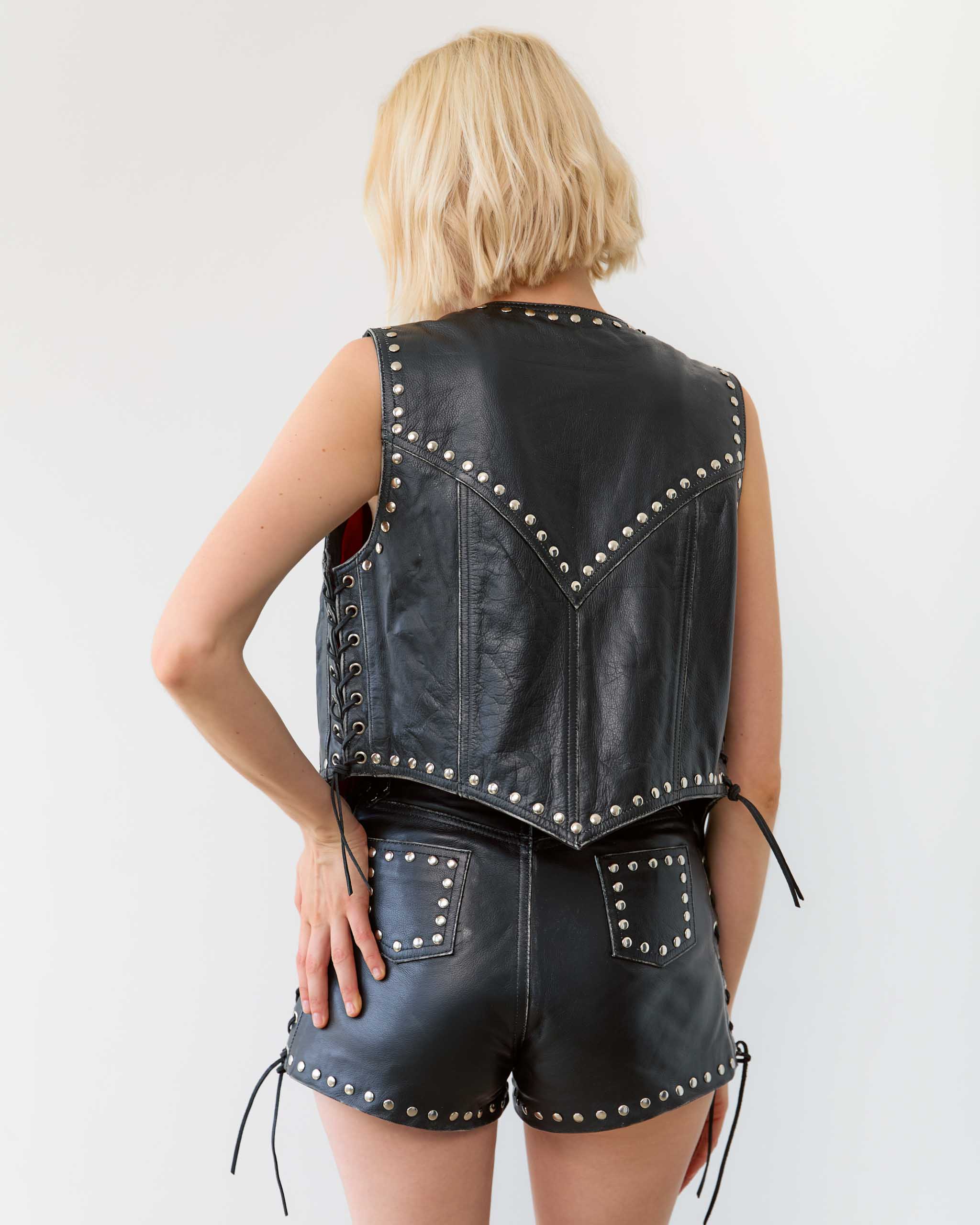 Person wearing a black leather vest with studs on a white background