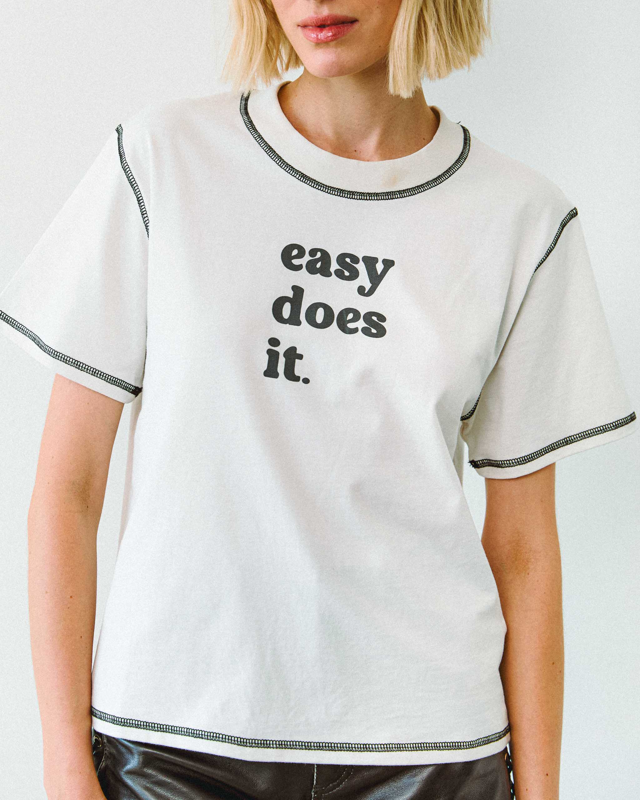Person wearing a white t-shirt with 'easy does it.' text on a plain background.
