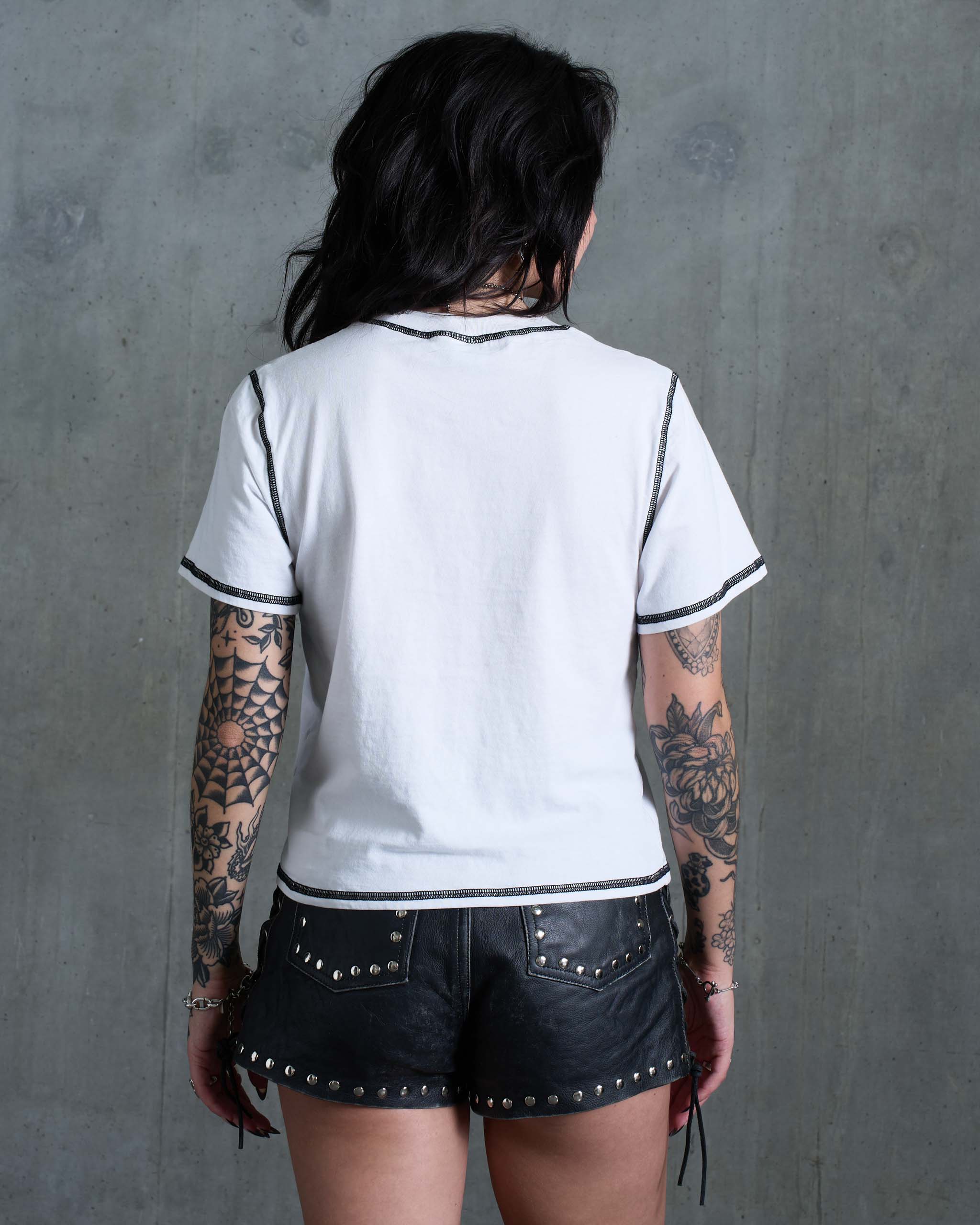 A tattooed woman wearing a white t-shirt with black contrast stitching, view from behind.
