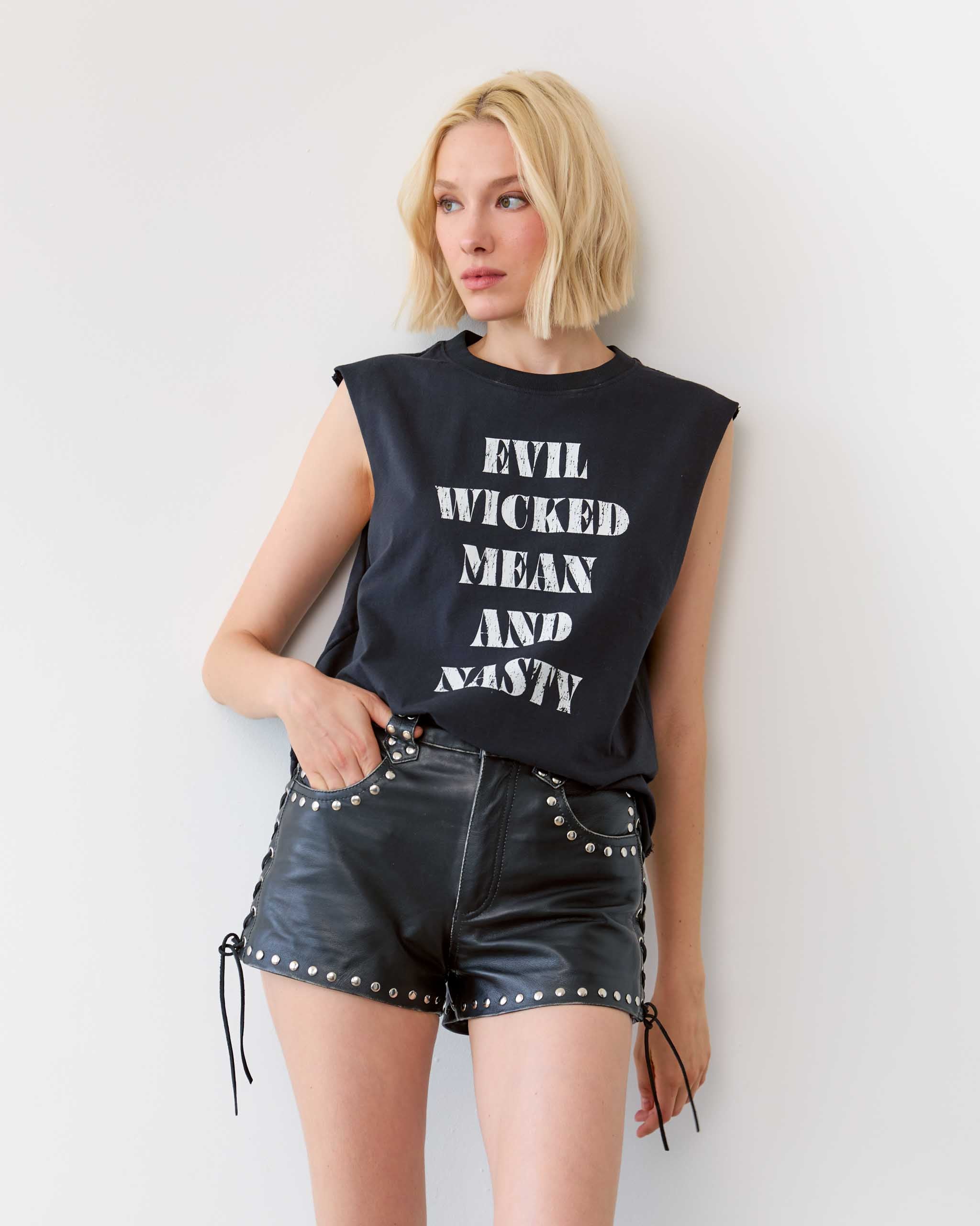 A woman wearing an 'Evil Wicked Mean And Nasty' sleeveless t-shirt, with some studded leather shorts.