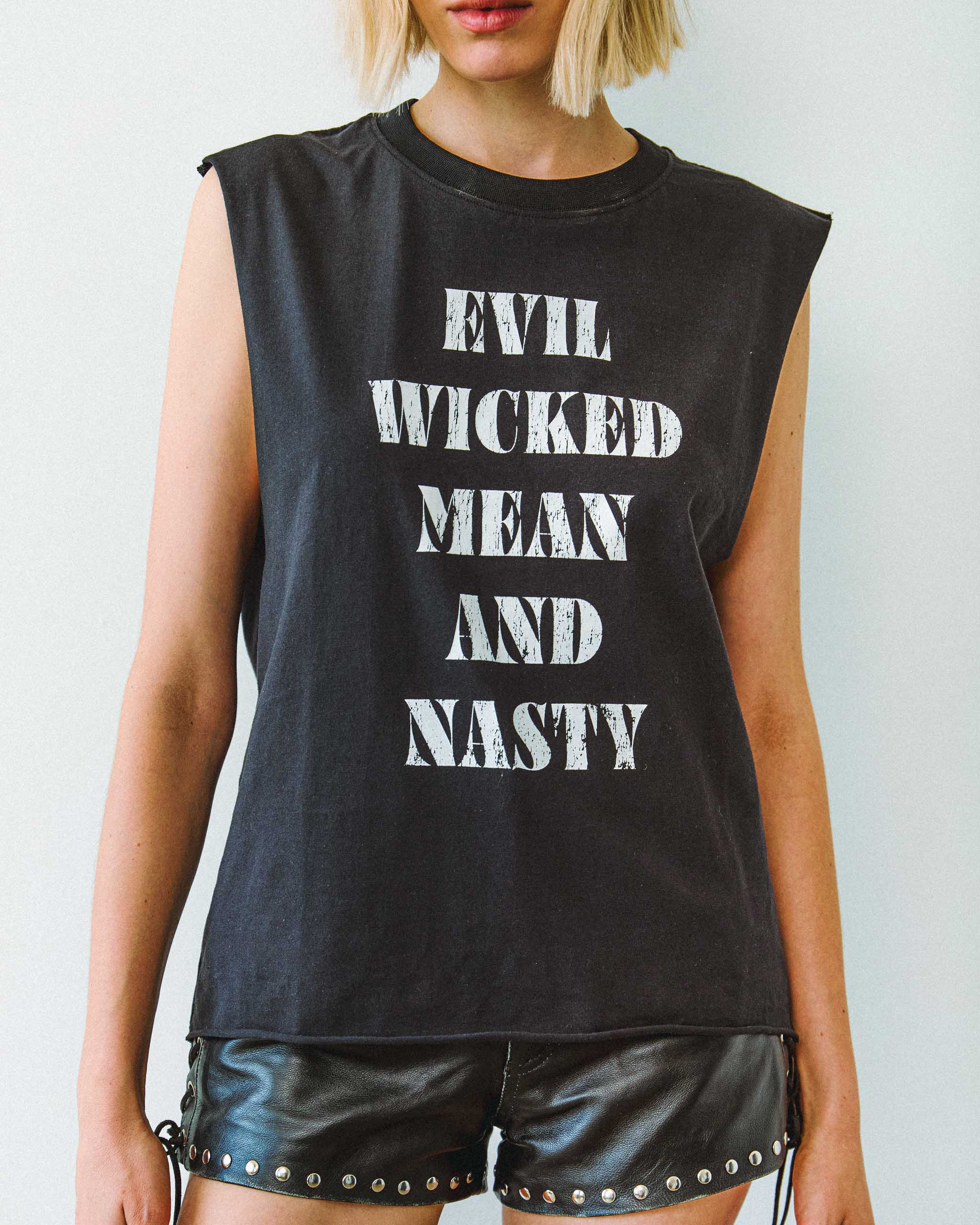 A biker model wearing an "Evil Wicked Mean and Nasty" sleeveless t-shirt and studded leather shorts.