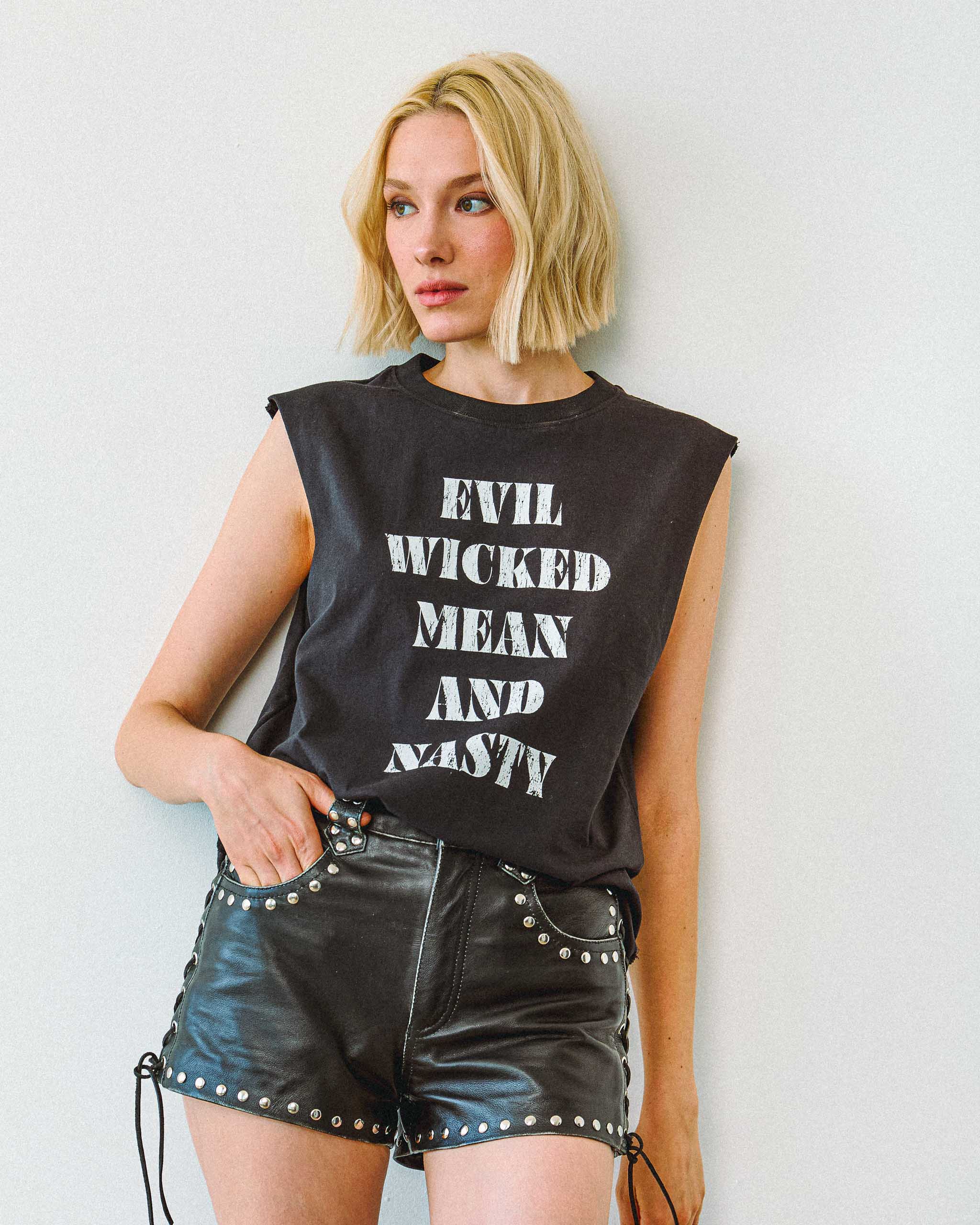 A gothic model wearing an "Evil Wicked Mean and Nasty" sleeveless t-shirt and studded leather shorts.