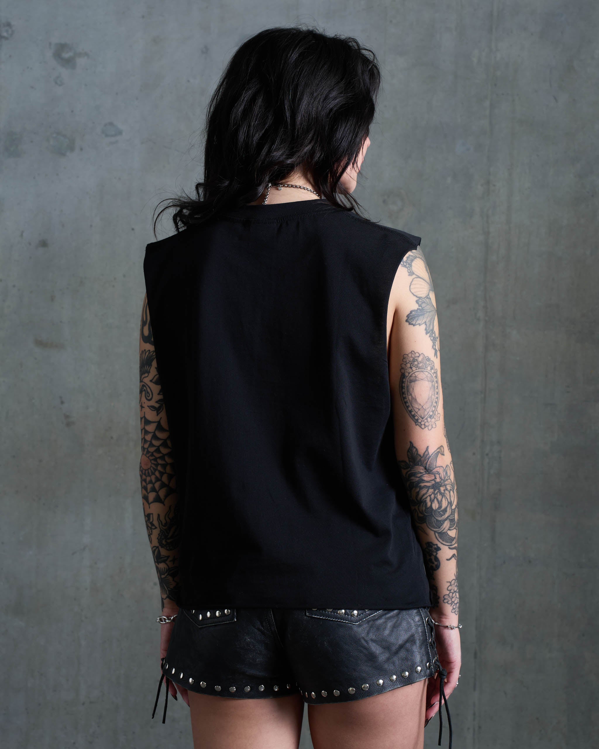 An alt woman wearing a black t-shirt with cut-off sleeves, view from behind.