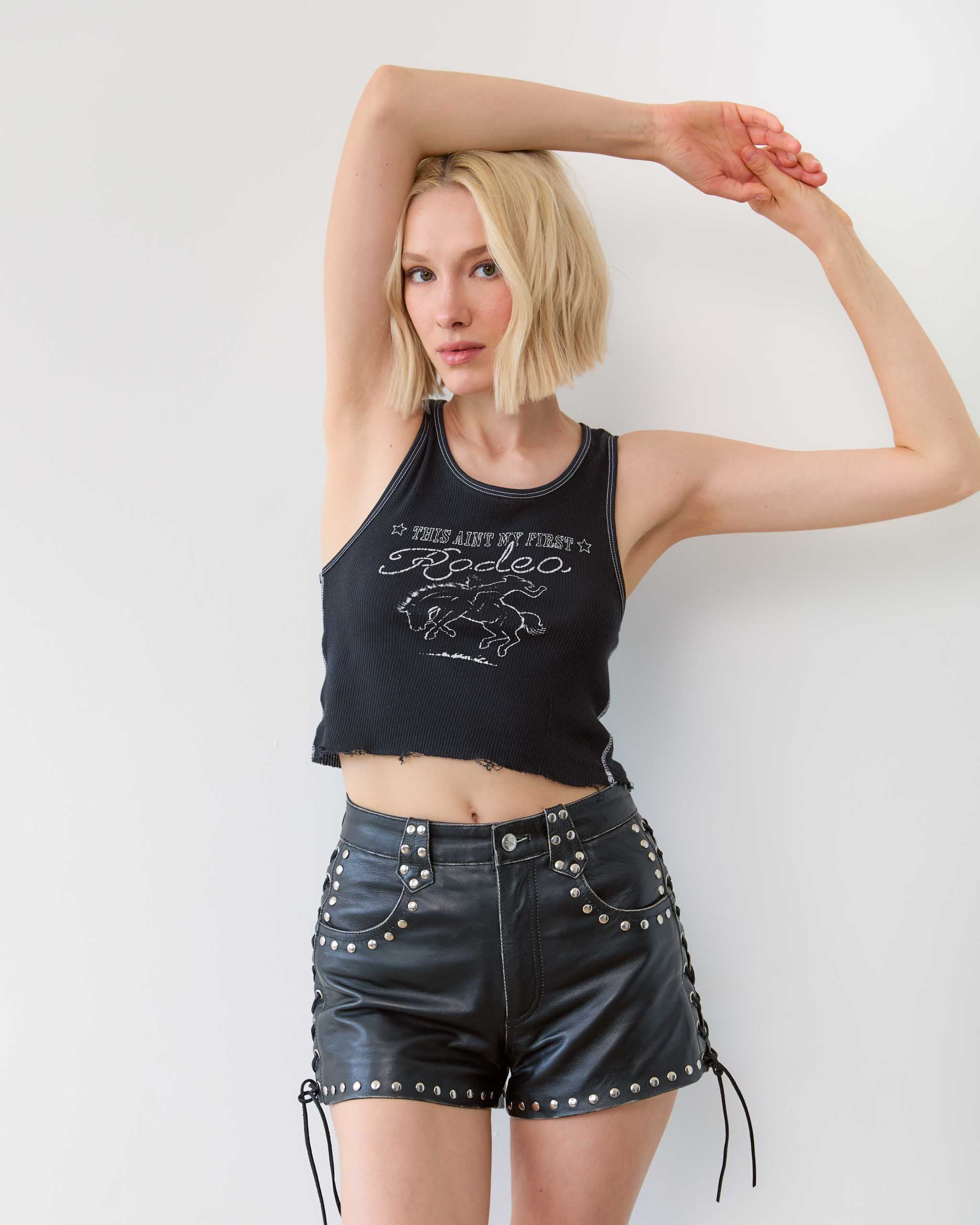 Woman wearing a black dark western tank top and studded black shorts on a white background