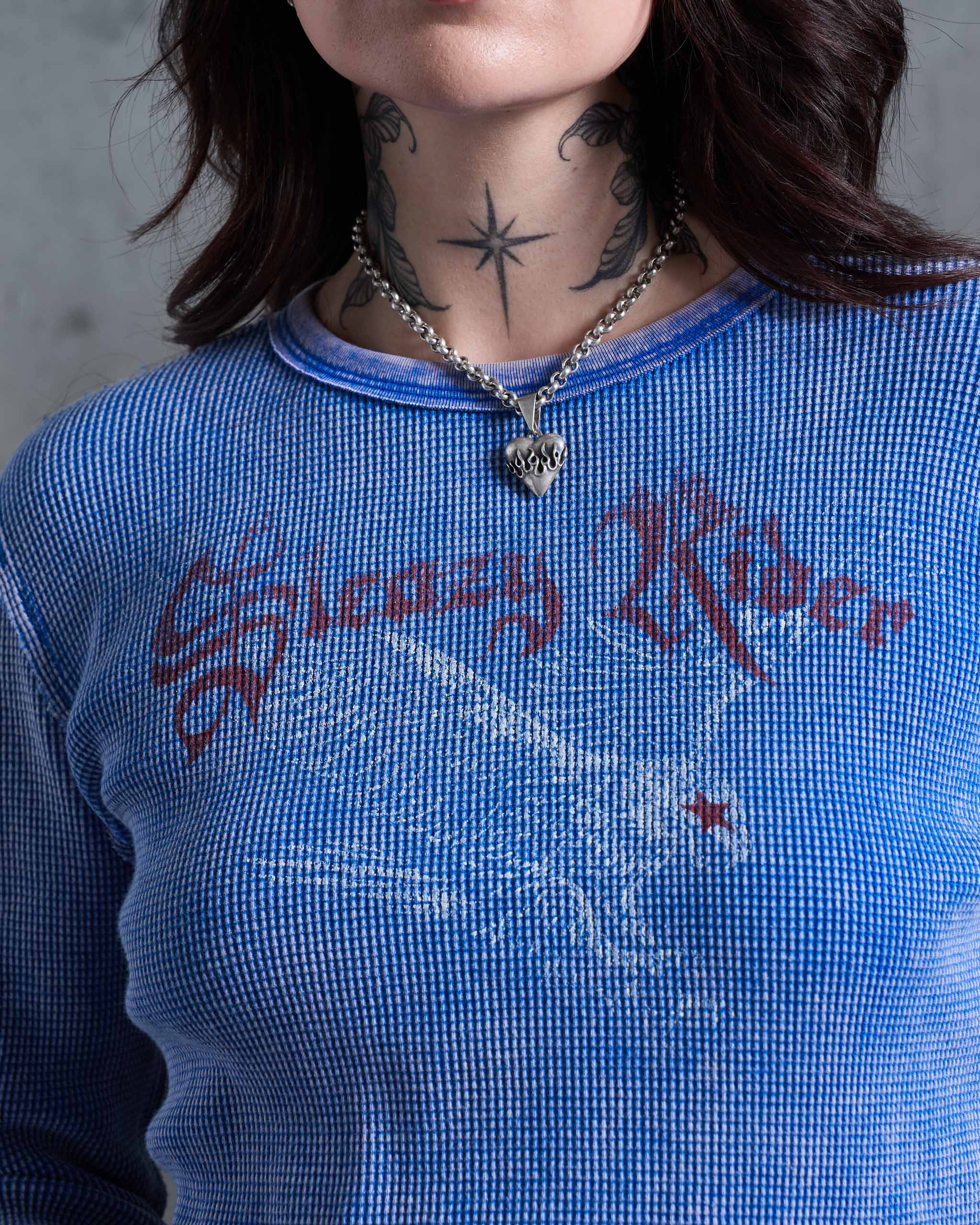 Close-up of a person wearing a blue faded vintage waffle knit top with 'Sleazy Rider' printed across the chest in dark red gothic lettering and a swooping eagle.