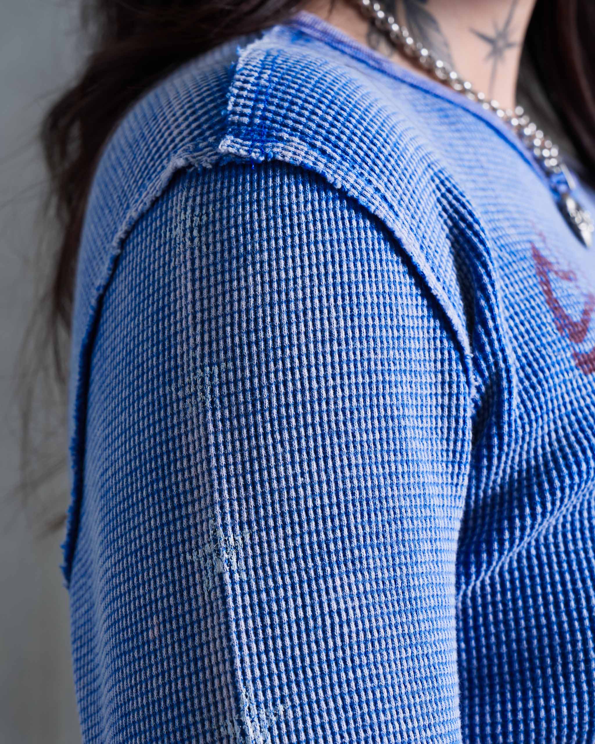 Close-up of a person wearing a faded blue waffle knit top, showing the shoulder raw edge seam.
