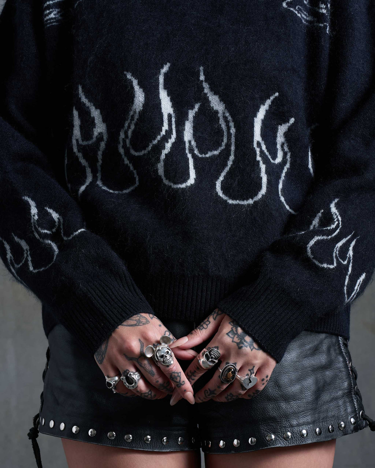 A knitted black sweater with flames on, worn by a tattooed woman with studded leather shorts.