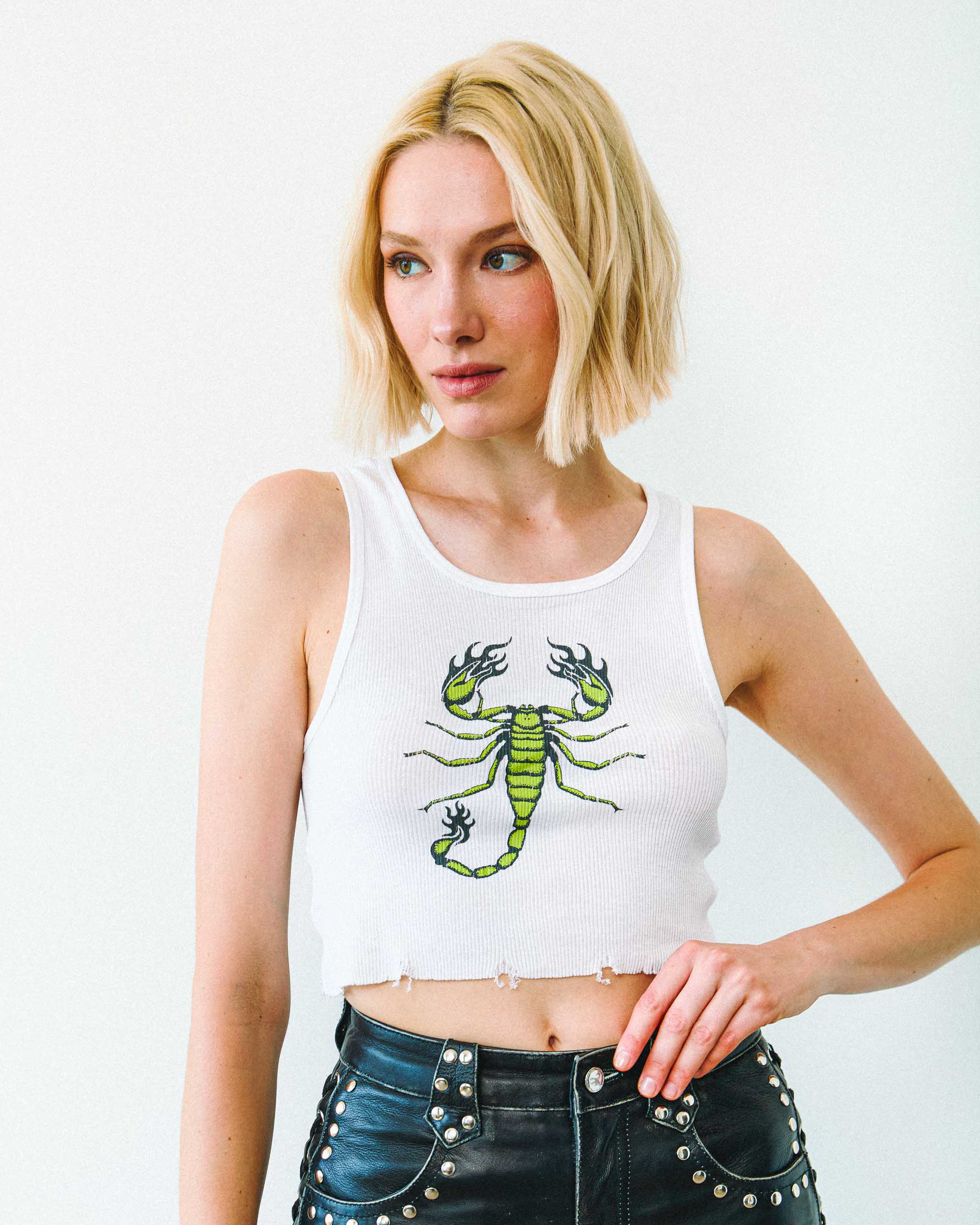 Woman wearing an alt tank top with green scorpion print and studded leather shorts on a plain background.