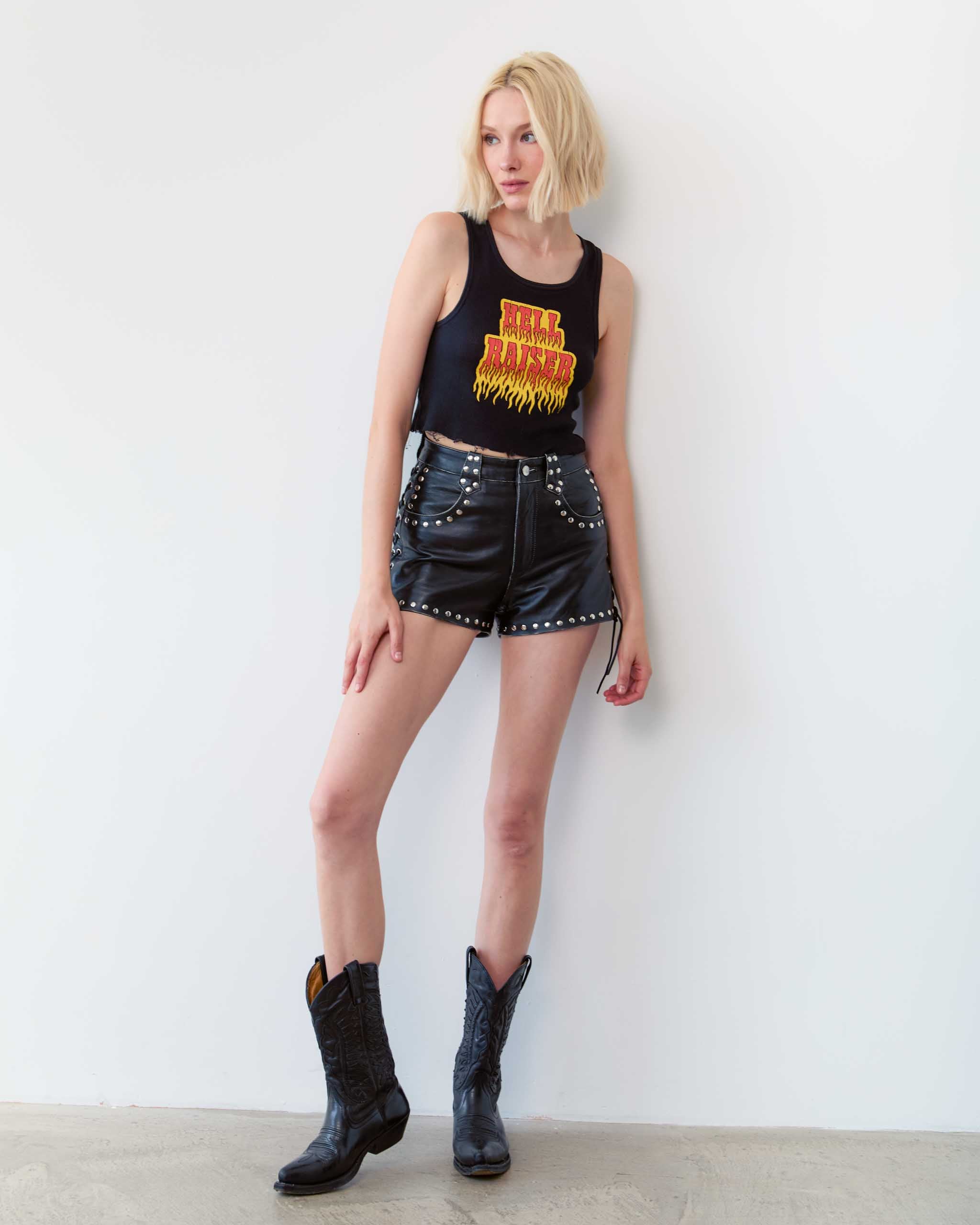 A dark western woman wearing a flaming Hell Raiser tank top and studded leather shorts.