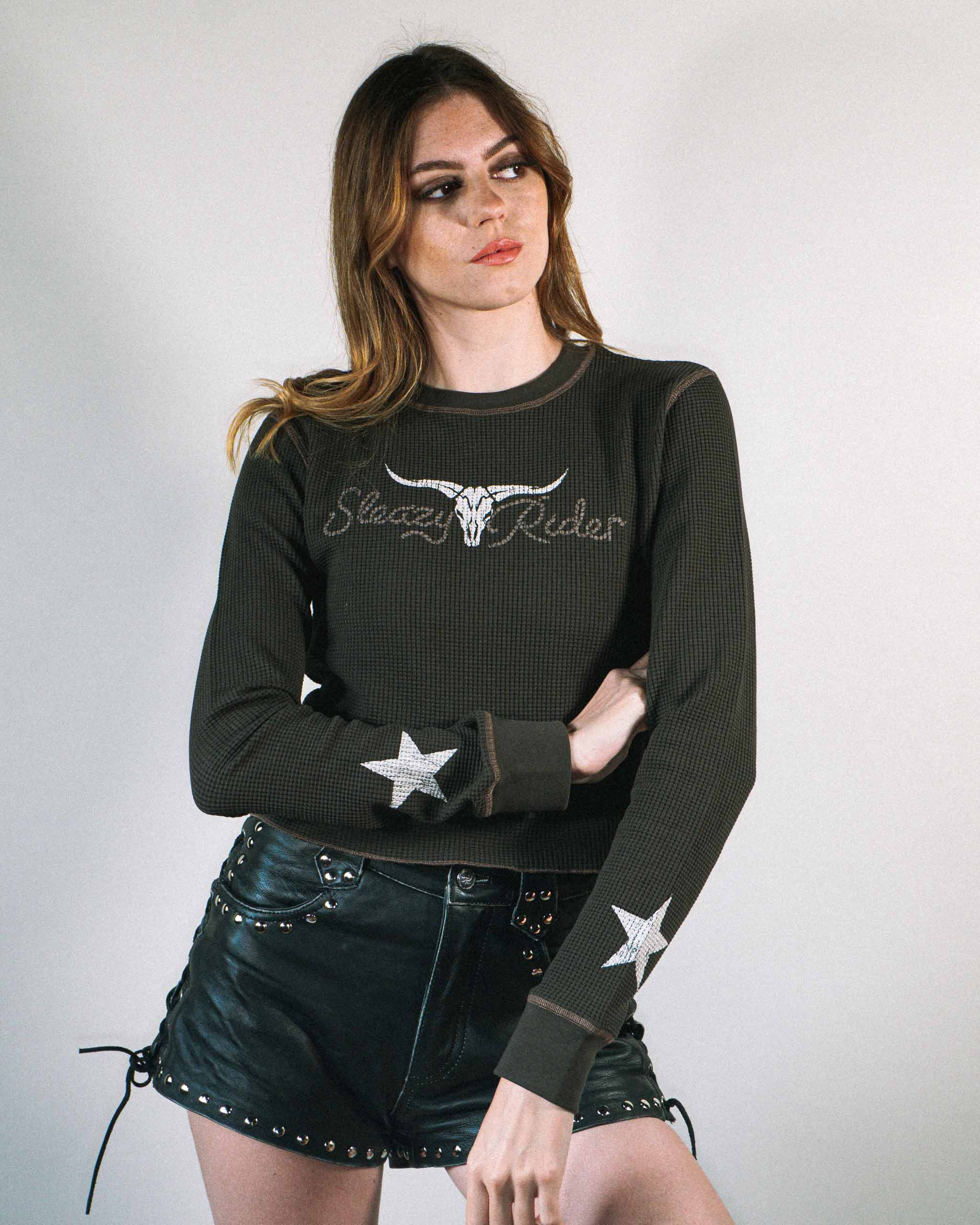 Woman wearing a gothic western waffle knit top with a cow skull on the font and stars on the sleeves.