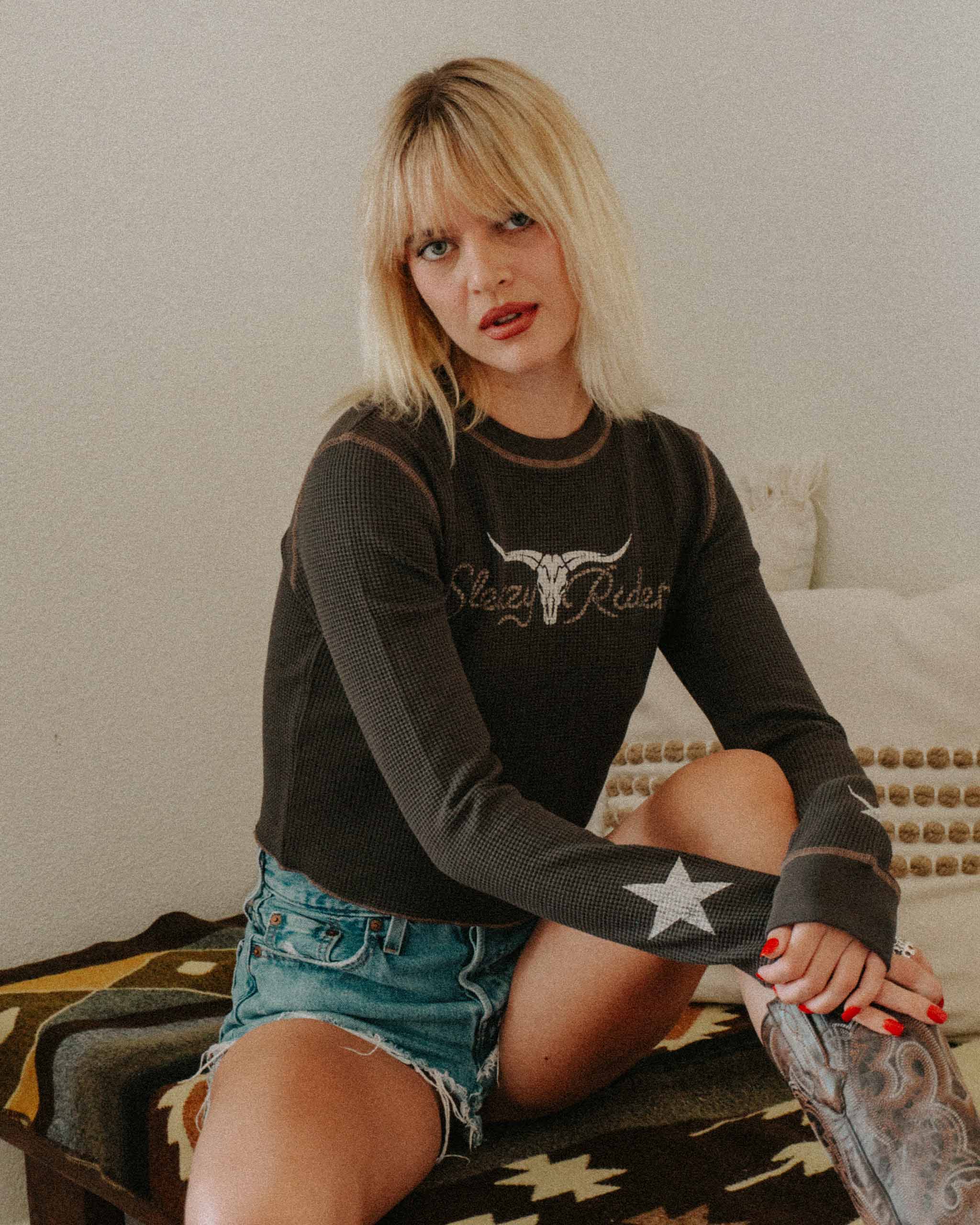 A woman wearing a black waffle knit top with a longhorn skull print on the front and stars on the sleeves.