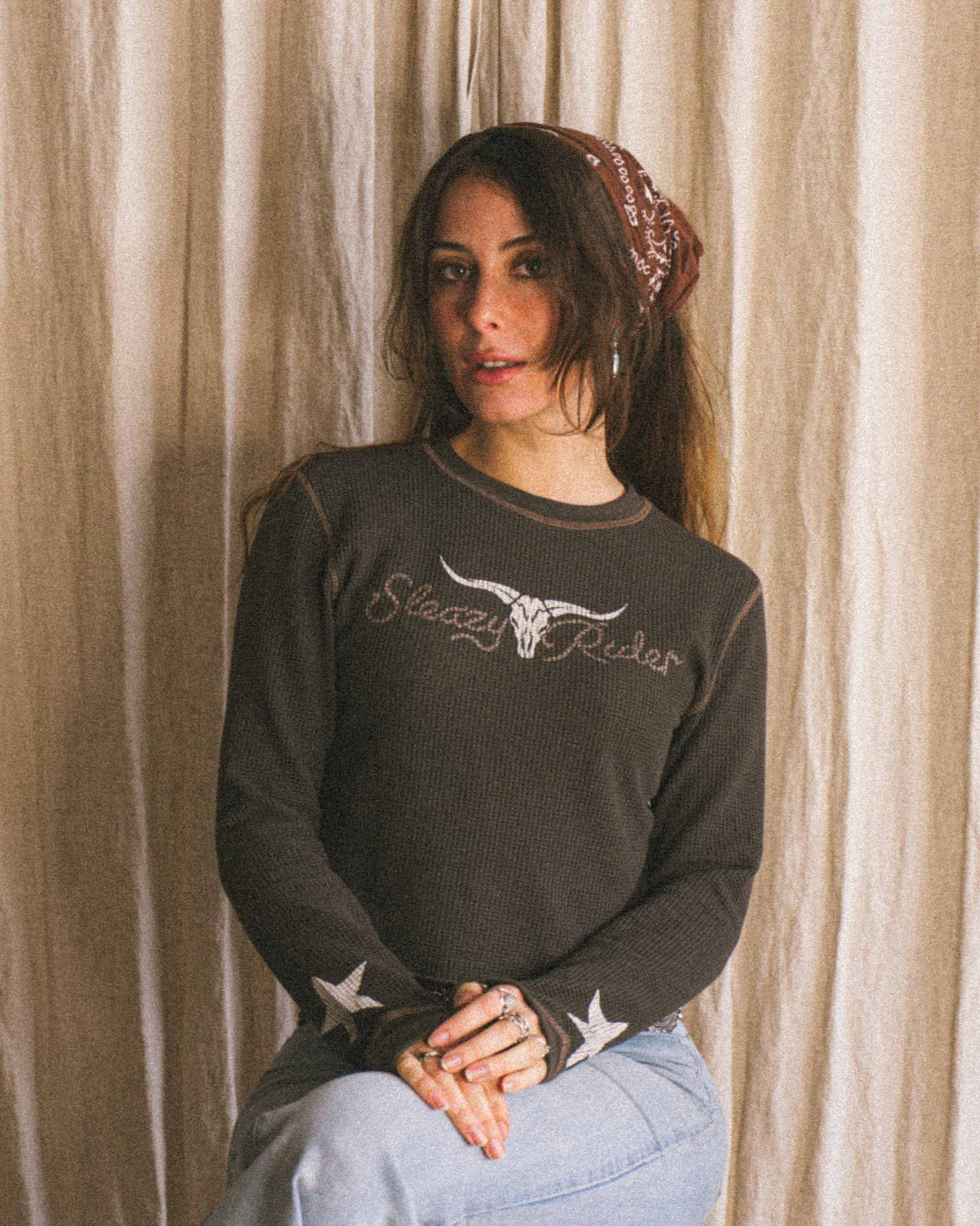 A woman wearing a long sleeve waffle knit top with a 'Sleazy Rider' Texas longhorn print and stars on the sleeves.