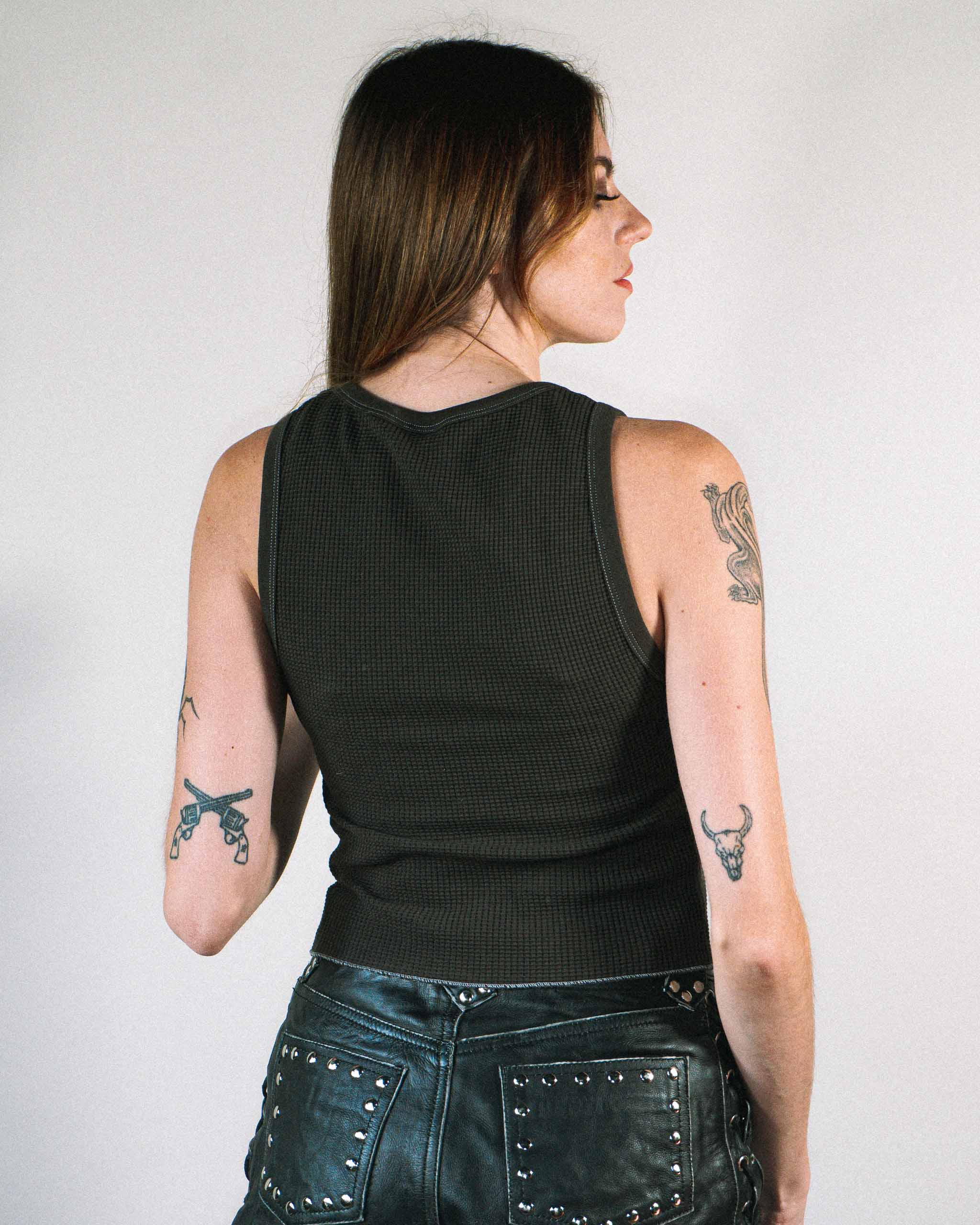Back view of a woman wearing a black waffle knit tank top and studded leather shorts.