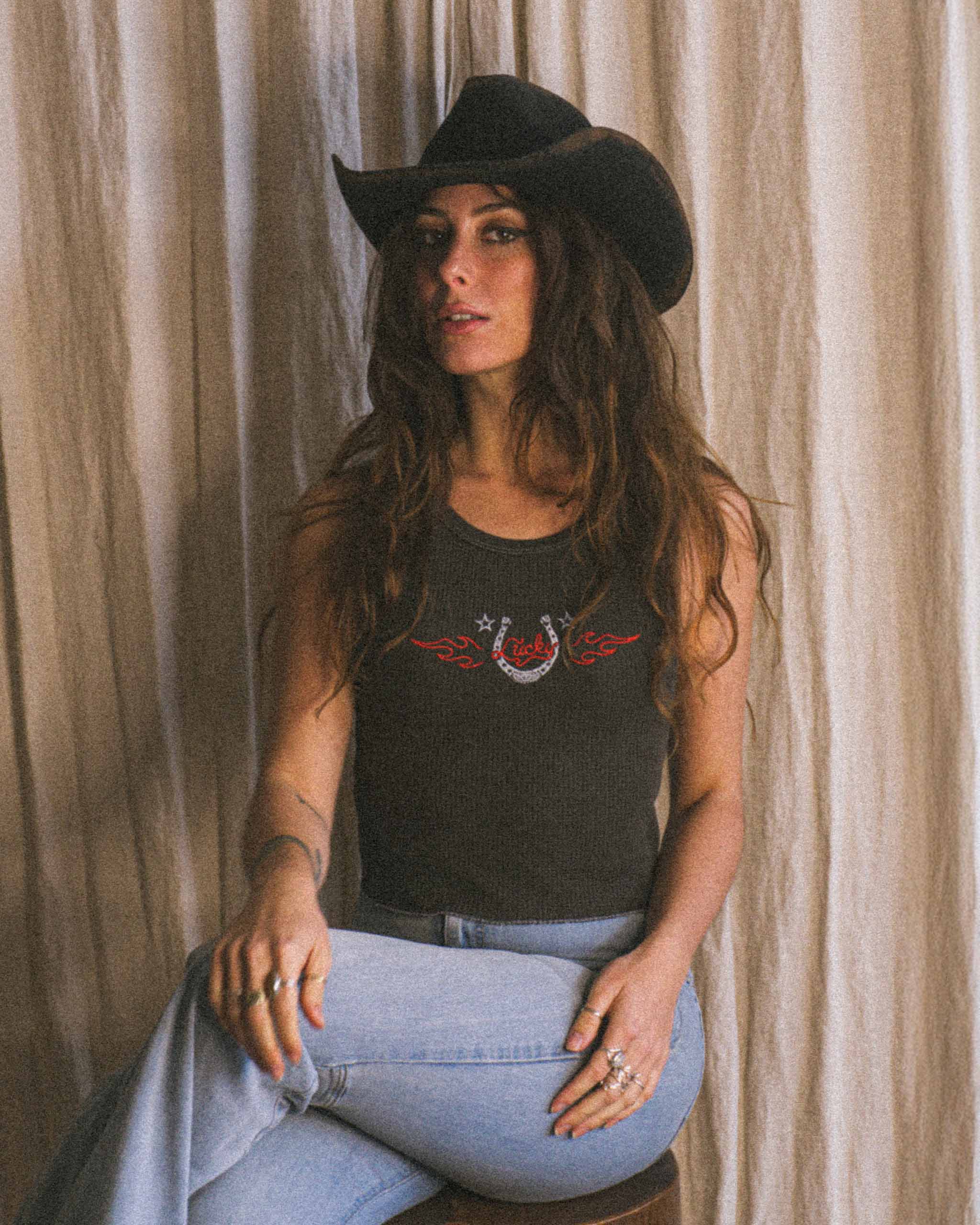 A cowgirl wearing a cowboy hat and a lucky horseshoe tank top.