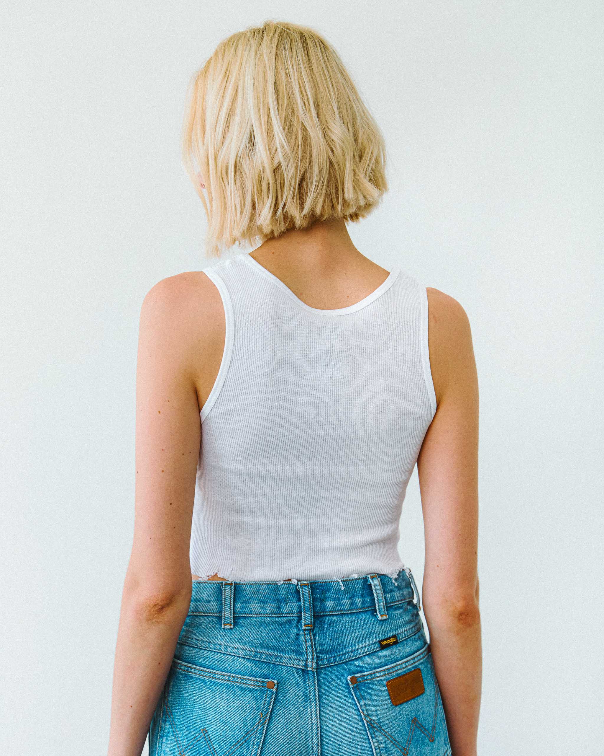 Woman wearing a white ribbed tank top and denim shorts.