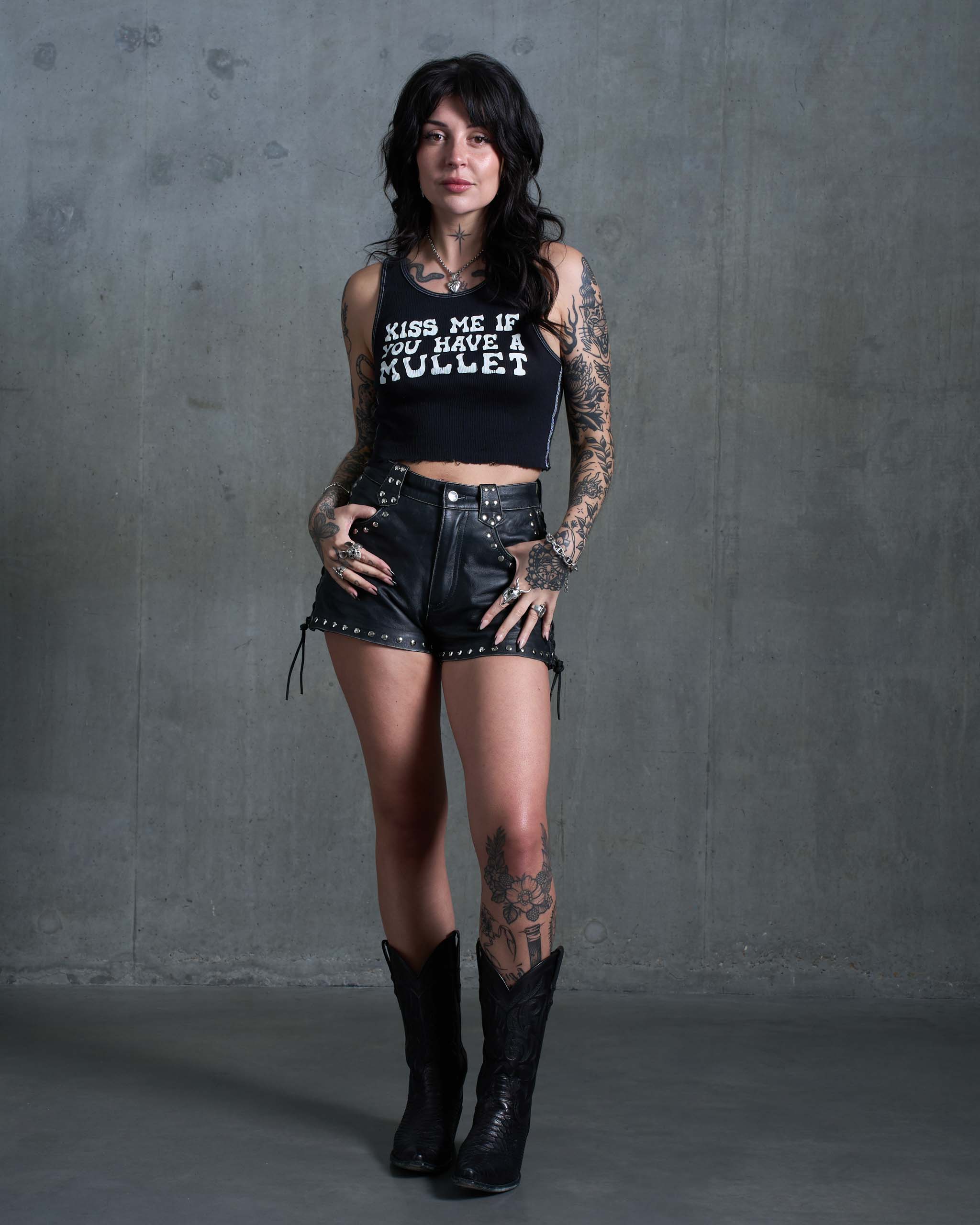 A sleazy woman wearing a "Kiss me if you have a mullet" tank top, with studded leather shorts and cowboy boots.