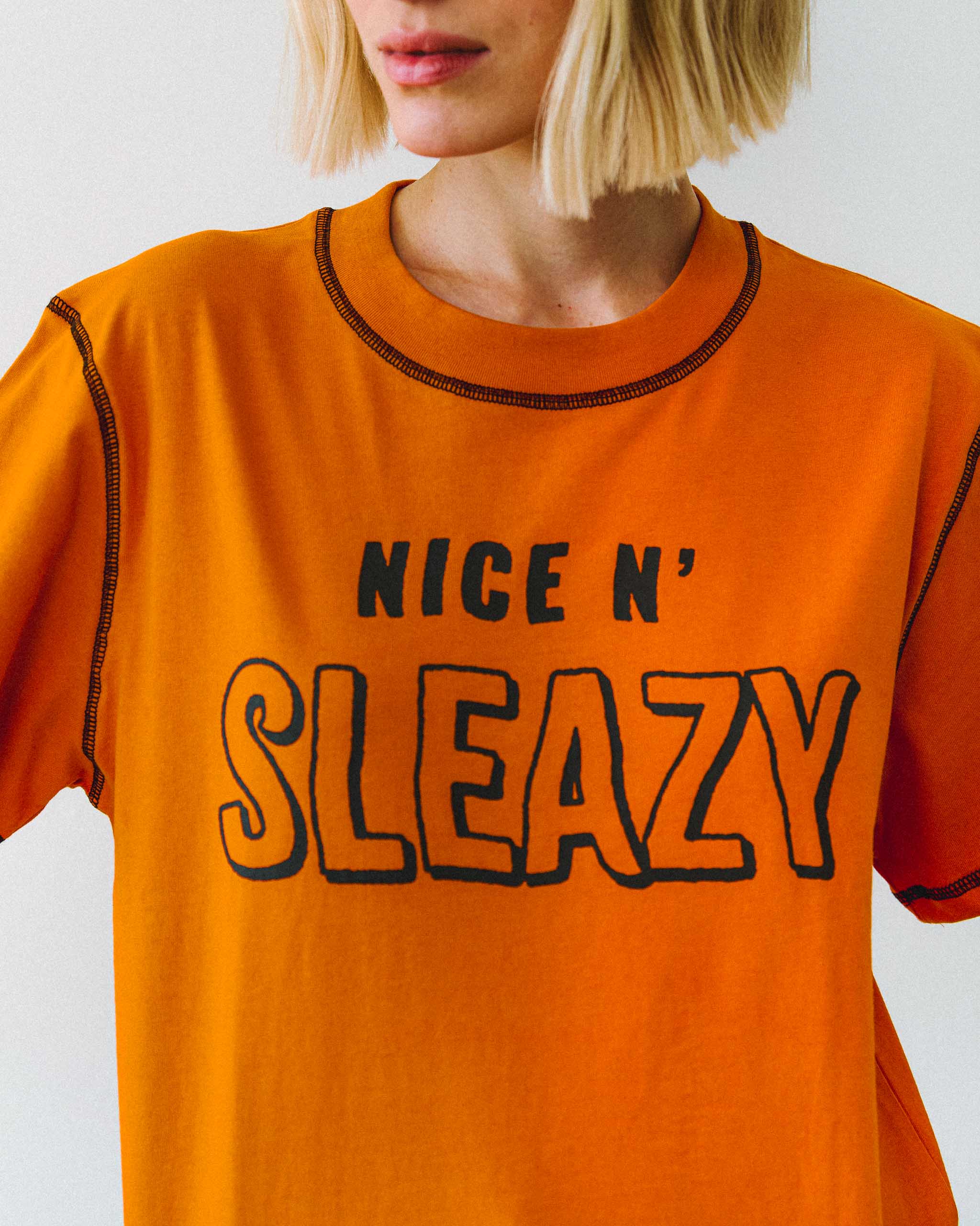 An orange "NICE N' SLEAZY" slogan t-shirt with black contrast stitching.