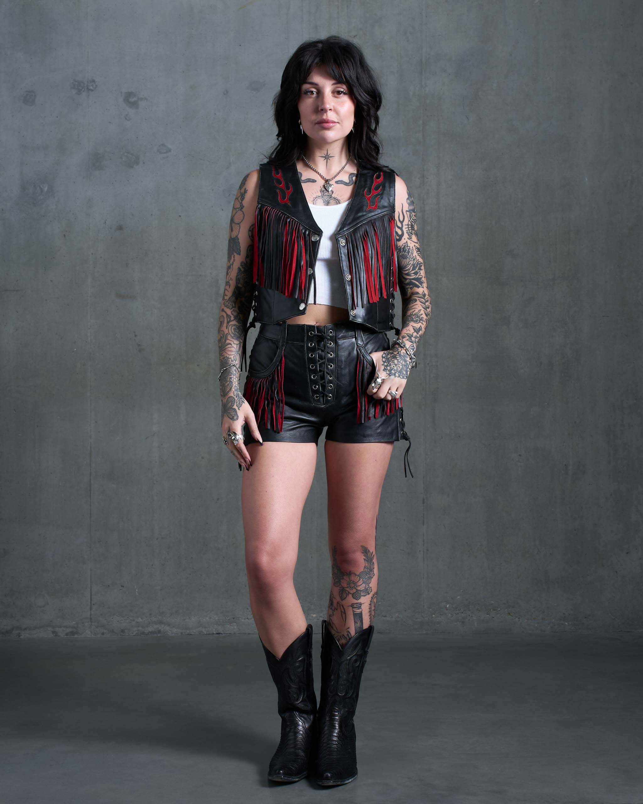 A tattooed biker model wearing a matching leather vest and shorts set.