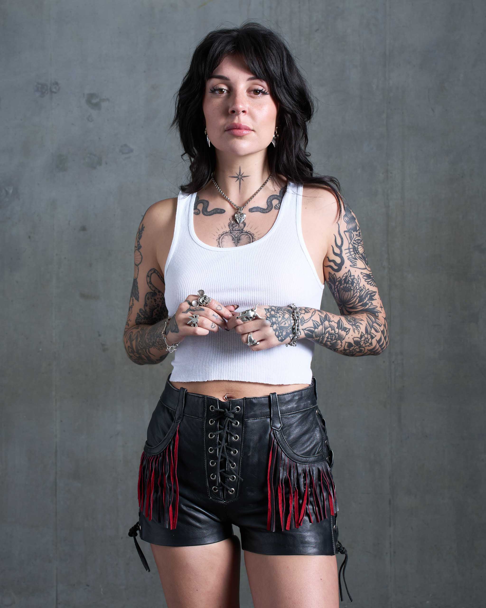 A tattooed model wearing lace-up biker shorts with red suede fringe.