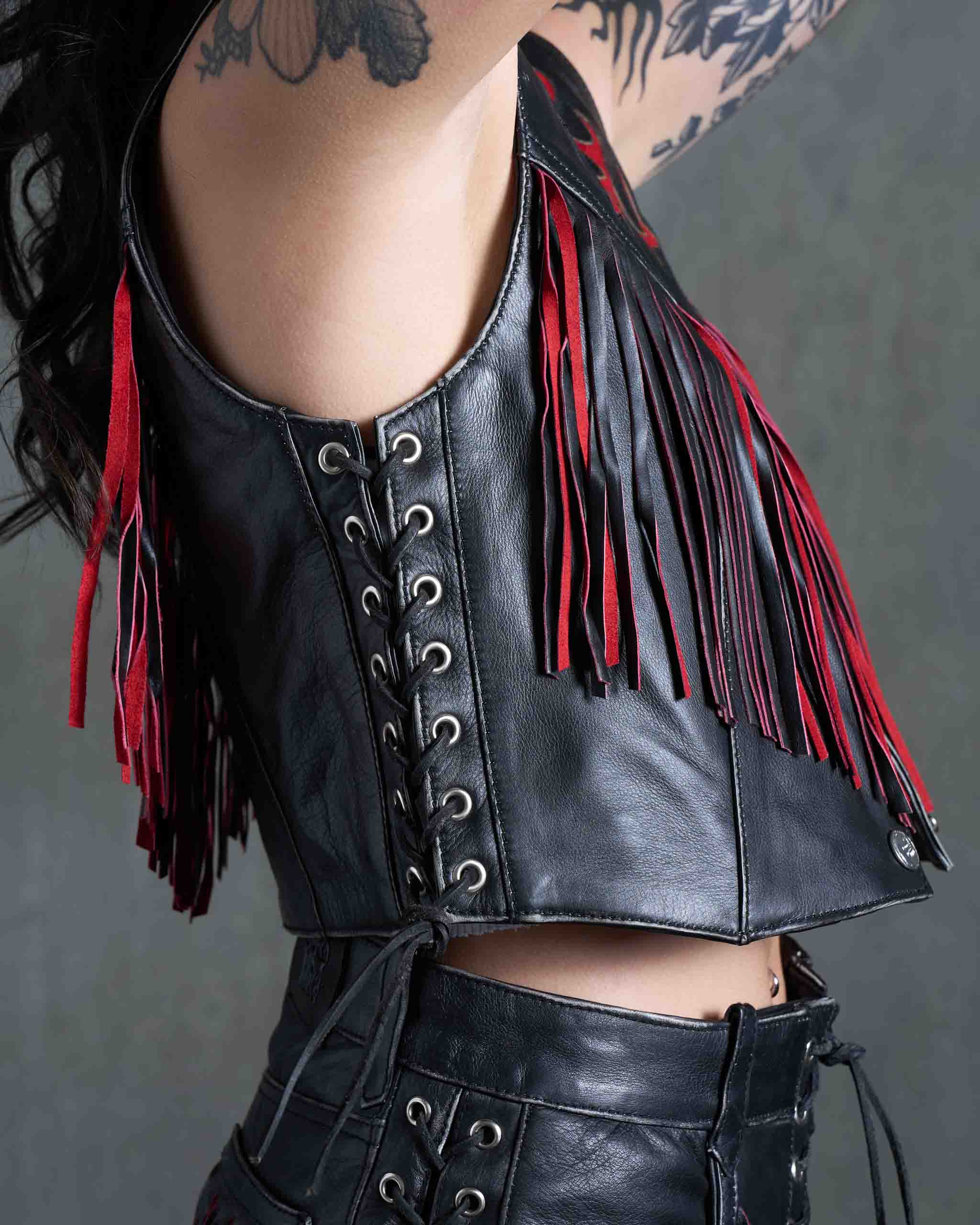 A biker model wearing a leather vest with lace-up sides and red suede fringe.