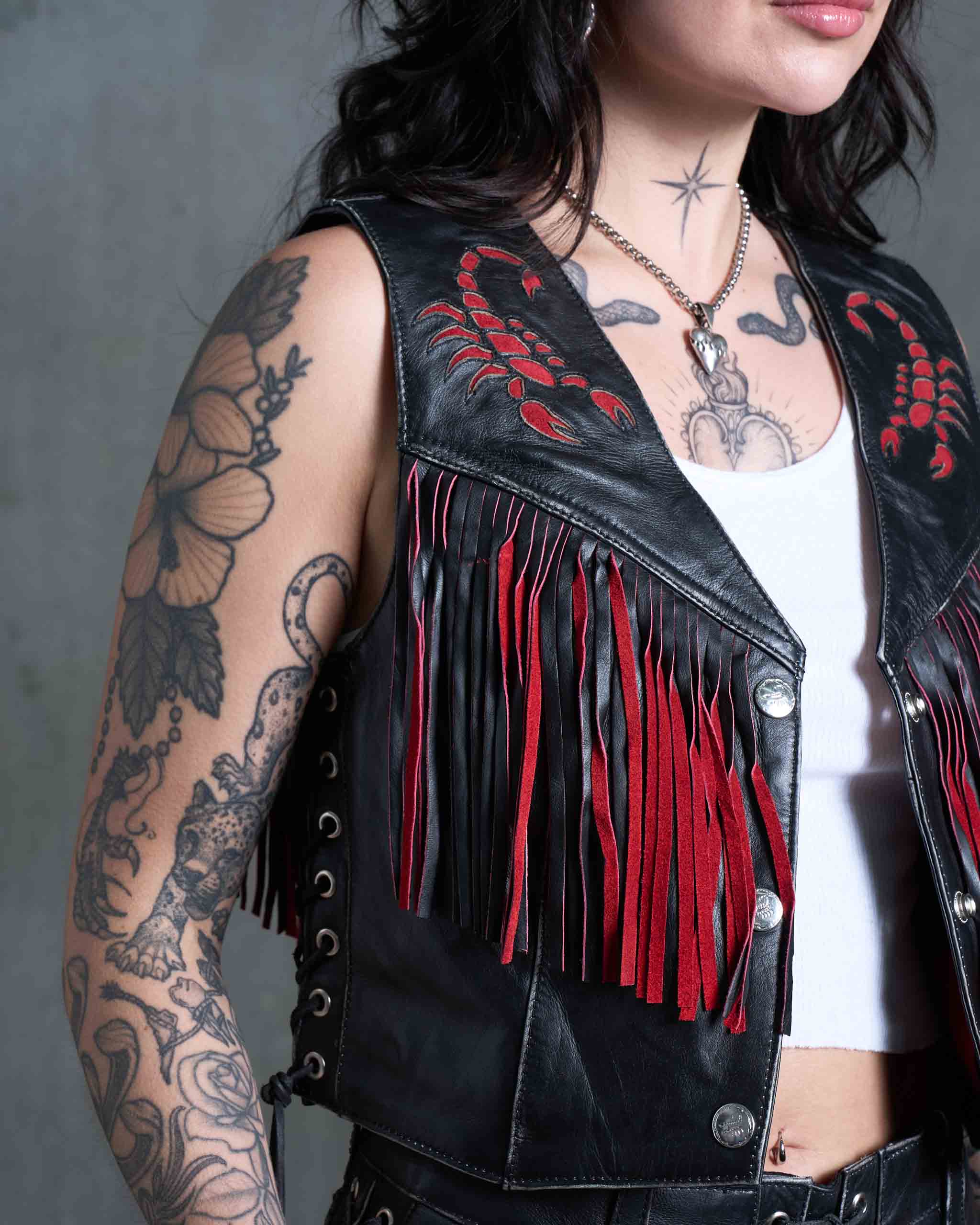 An up-close shot of red suede scorpion details on a black leather women's biker vest.