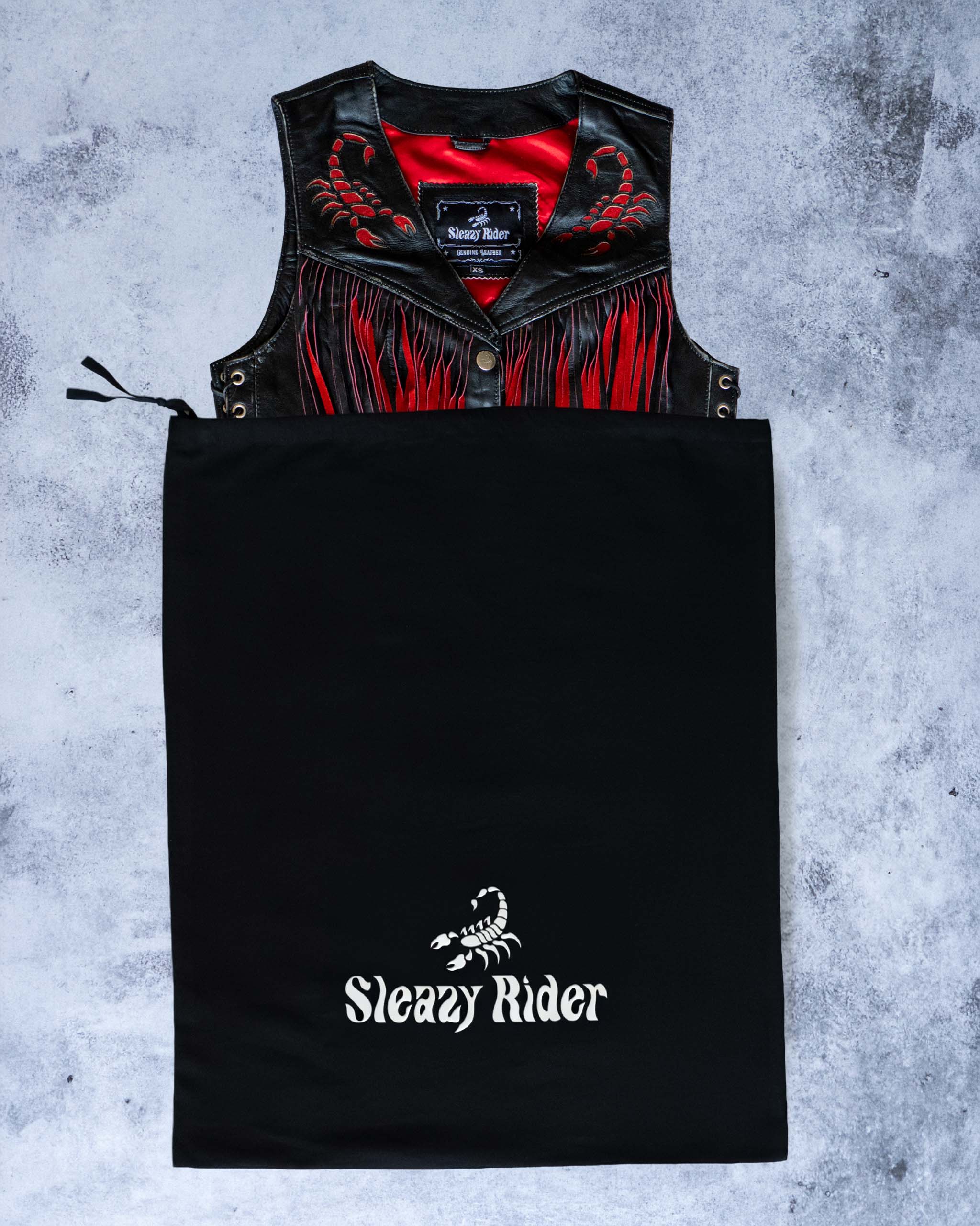 A black leather biker vest with scorpion details, coming out of a Sleazy Rider dust bag.