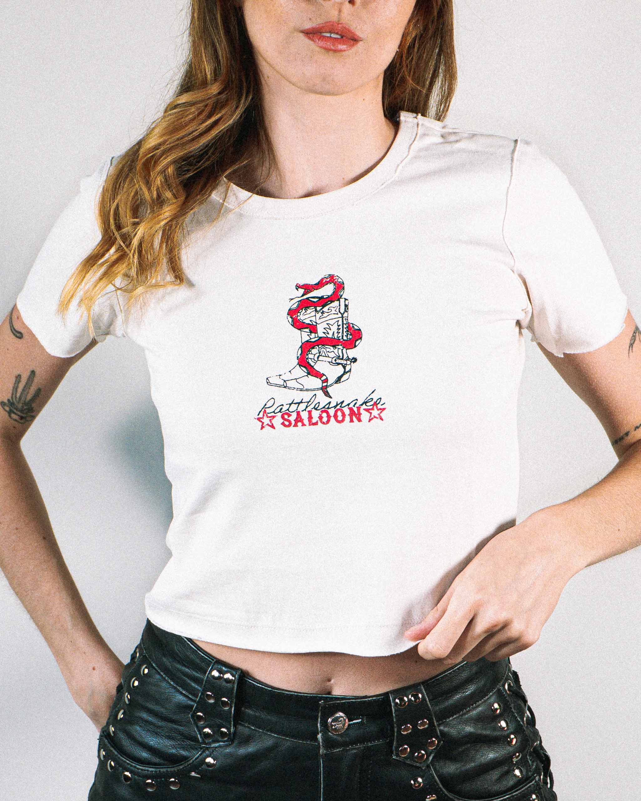 A model wearing a baby t-shirt with a rattlesnake and cowboy boots print on the front.