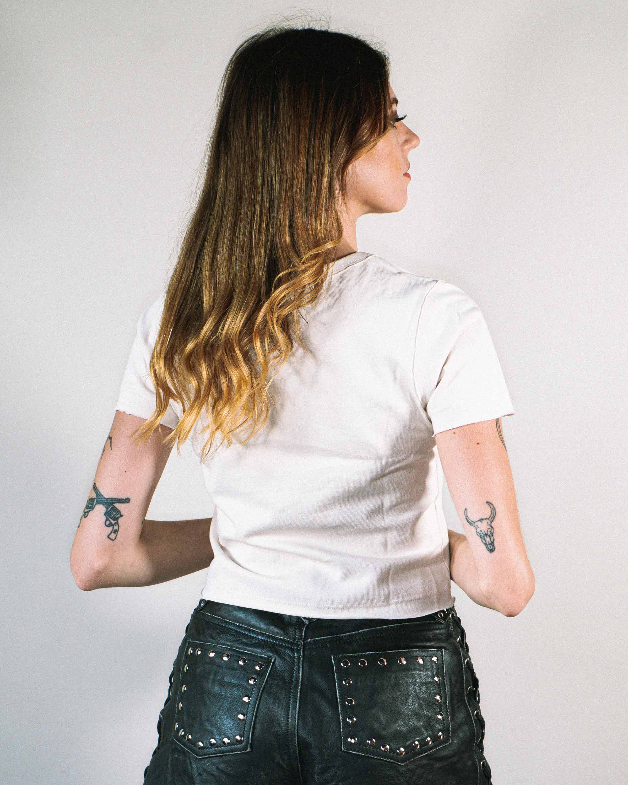 Back view of a woman wearing a white baby t-shirt and studded leather shorts.