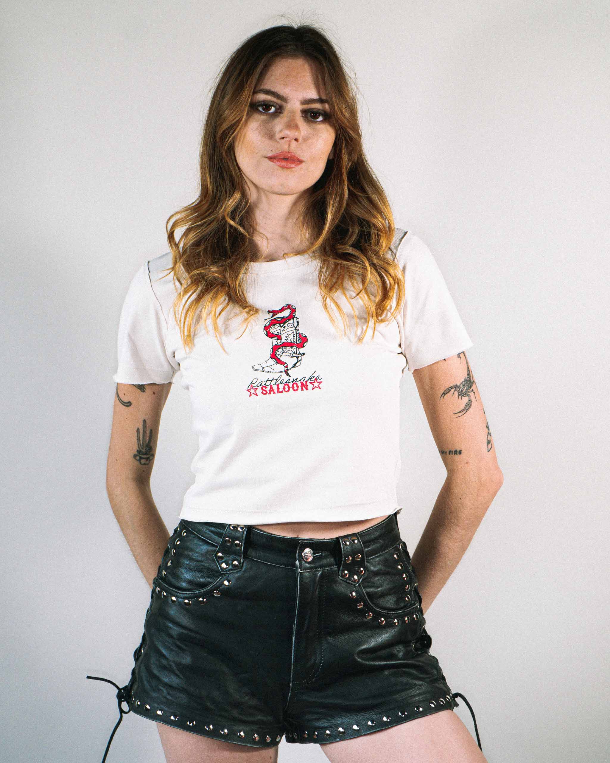 A woman wearing a baby t-shirt with a rattlesnake and cowboy boots print on the front.