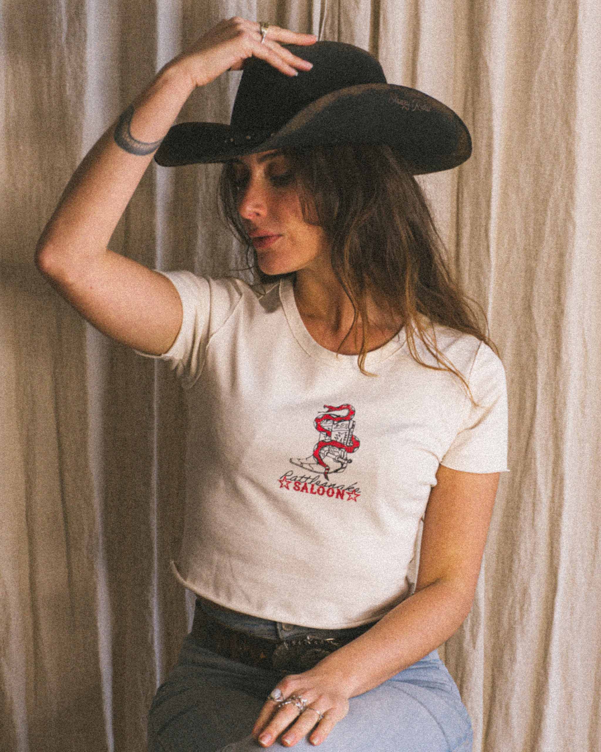 A cowgirl wearing a cowboy hat and a rattle snake pint baby tee.