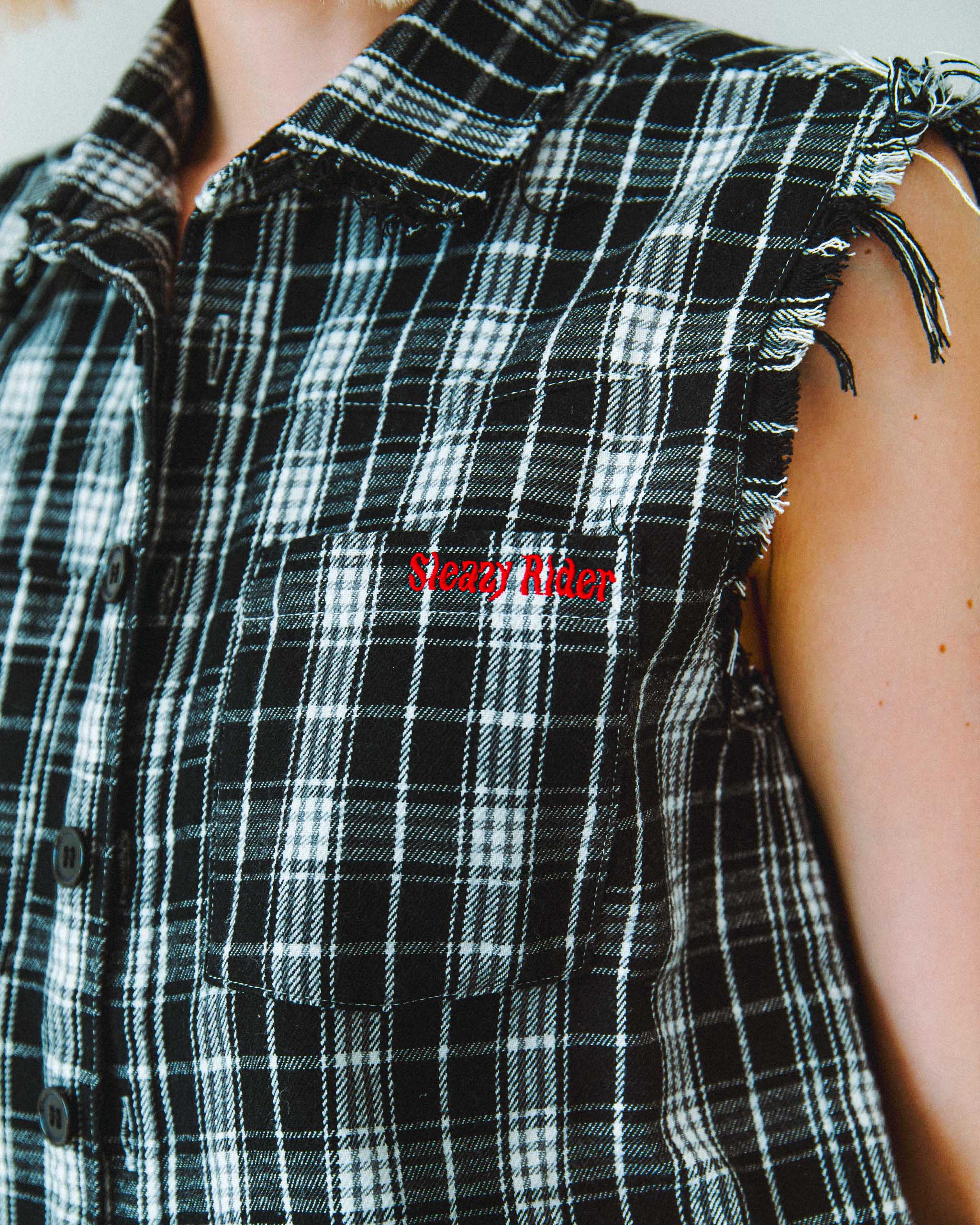Black and white plaid shirt with raw hems and a red embroidered 'Sleazy Rider' logo.
