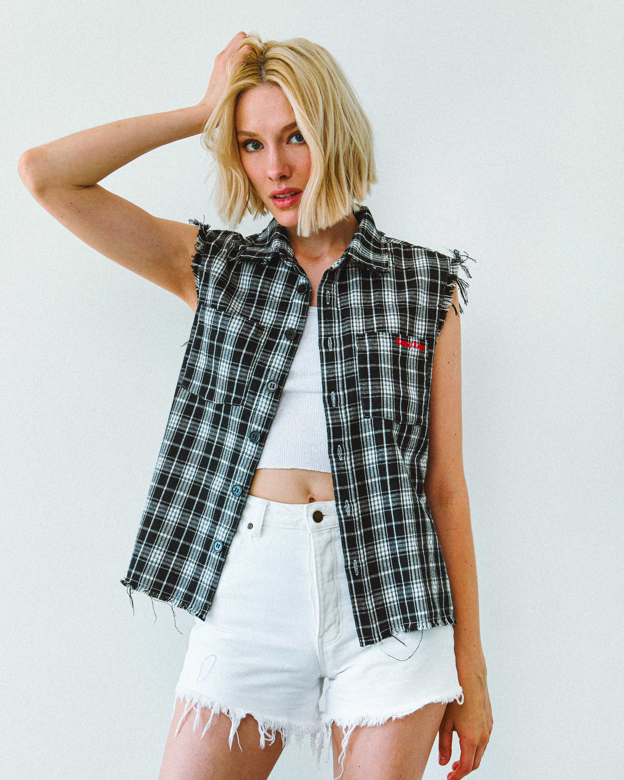 A female model wearing a black and white biker flannel sleeveless shirt, with Sleazy Rider embroidery.