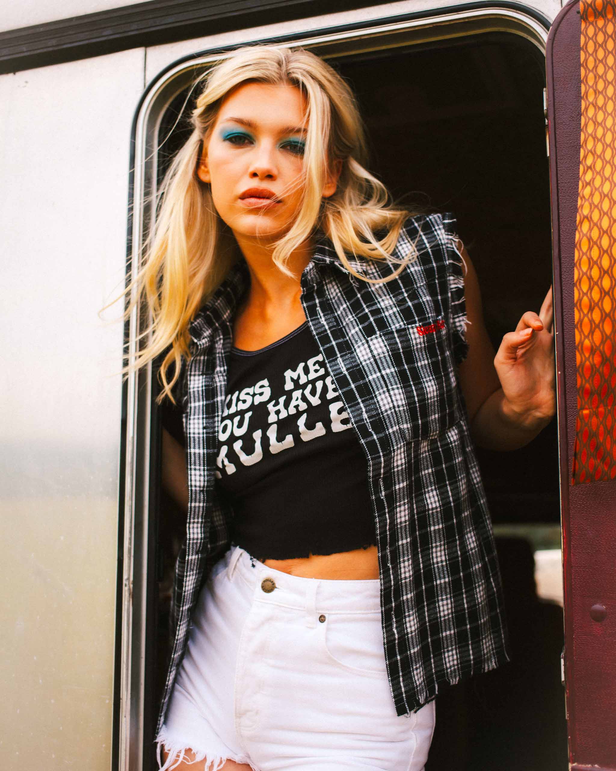 Woman standing in a vehicle doorway wearing a black graphic mullet tank top and Sleazy Rider Rowdy flannel shirt.