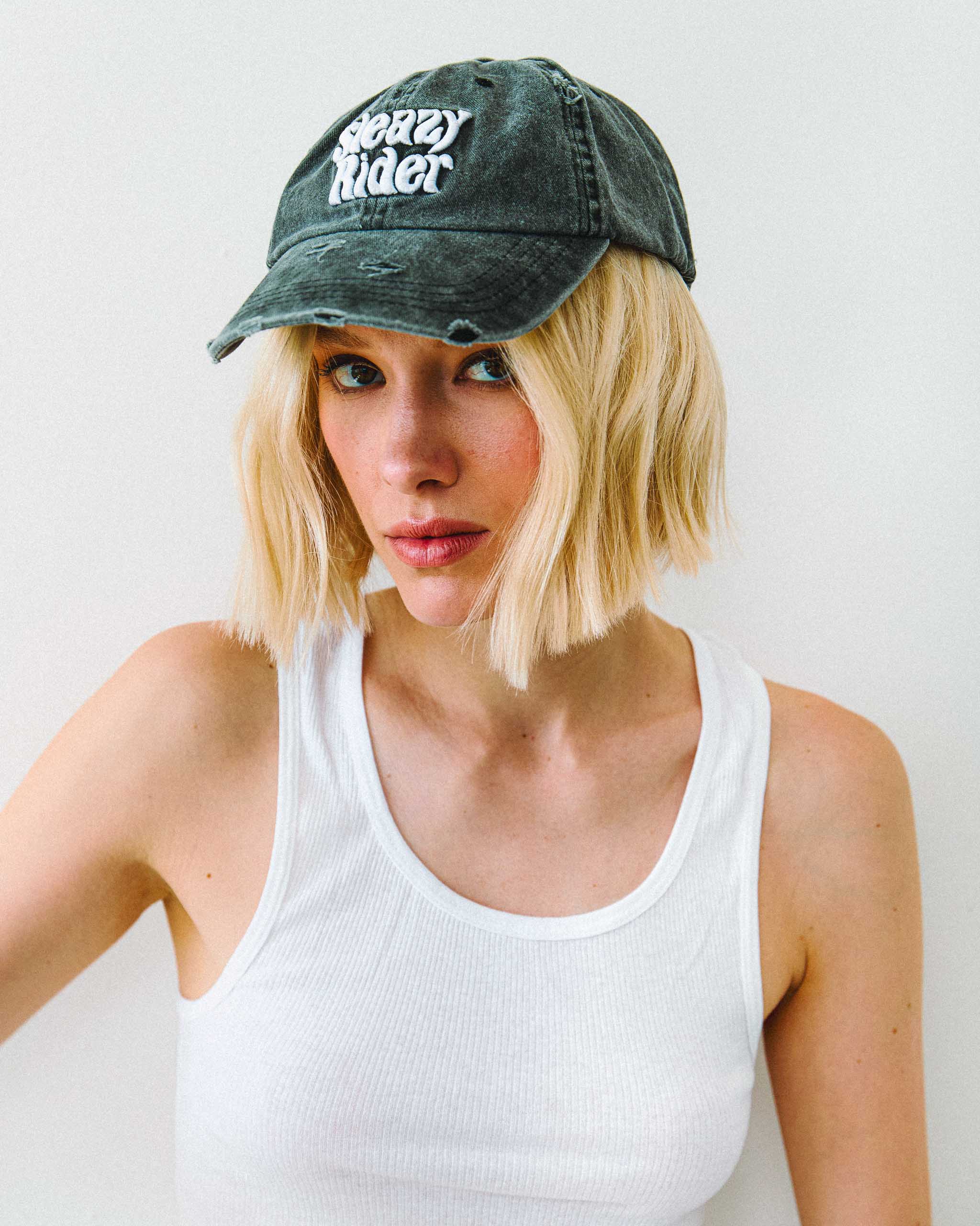 Model wearing an acid wash vintage style cap with "Sleazy Rider" embroidery.
