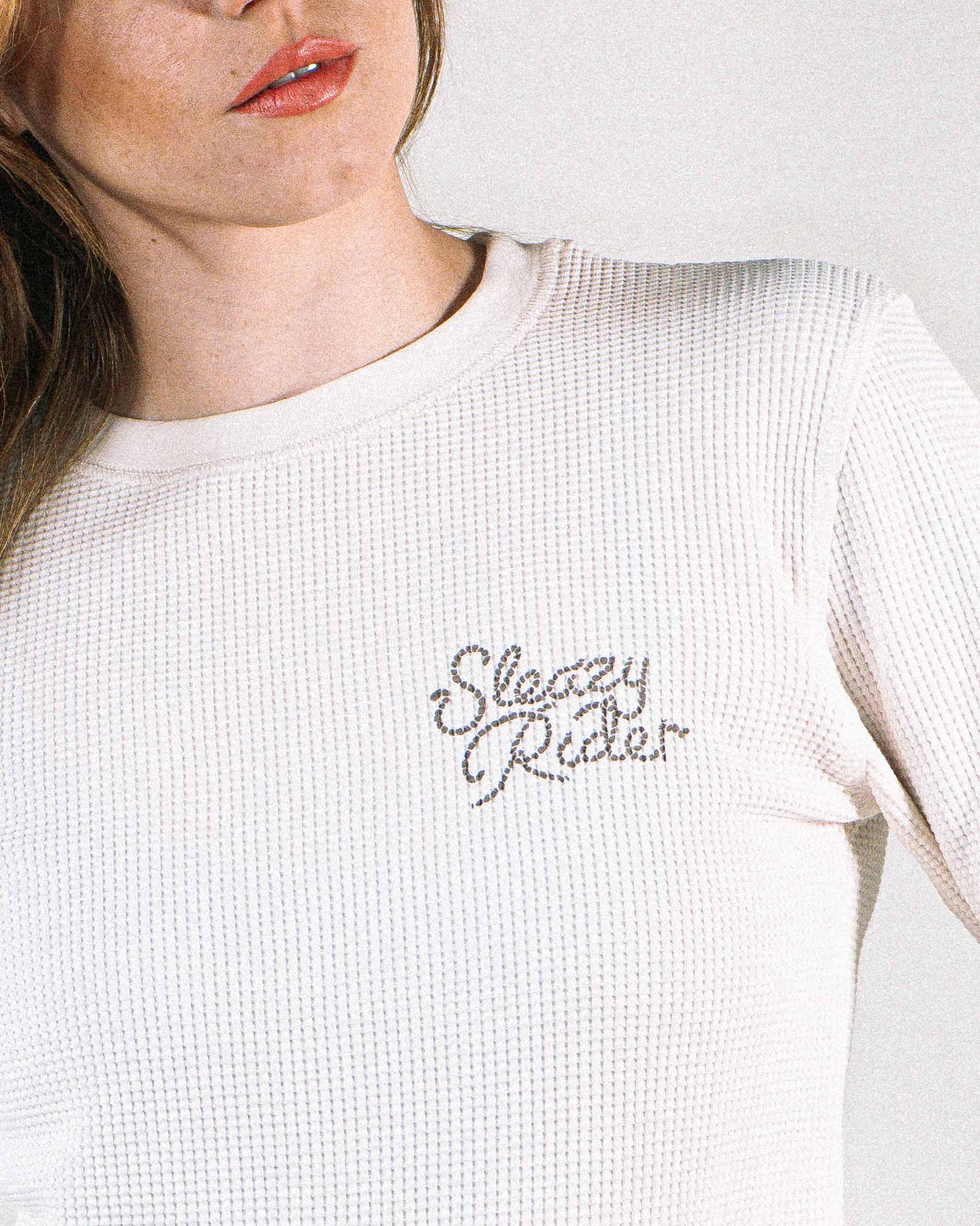 Woman wearing an off white waffle knit top with Sleazy Rider rope text