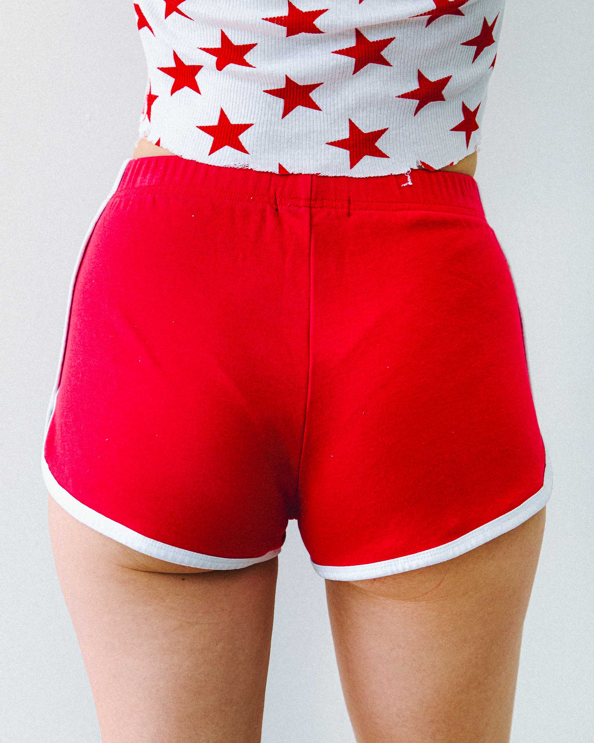 Model wearing red 80s gym shorts made by Sleazy Rider, on a light background.