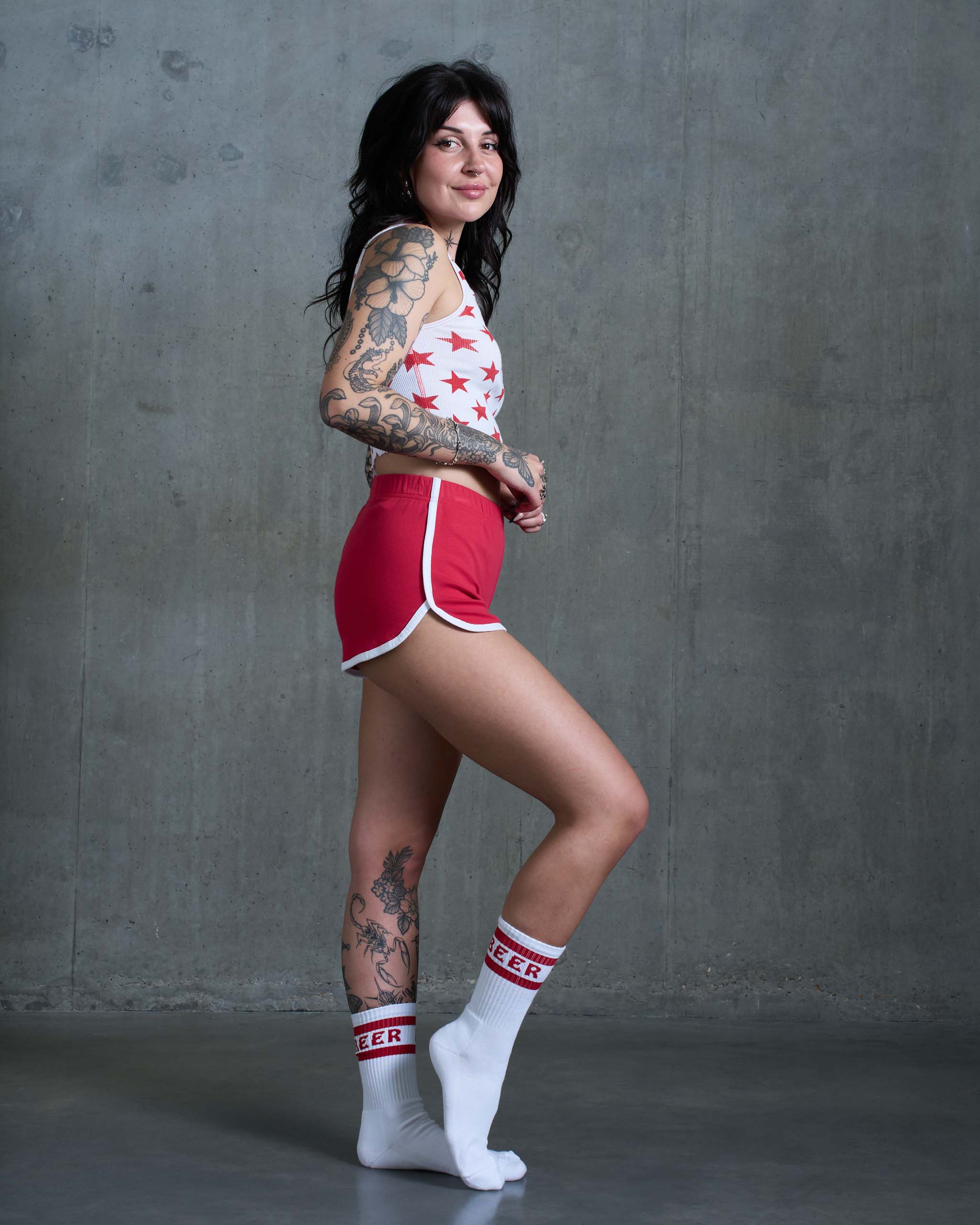A tattooed woman wearing some vintage 80's sports shorts with a star print top and white socks.