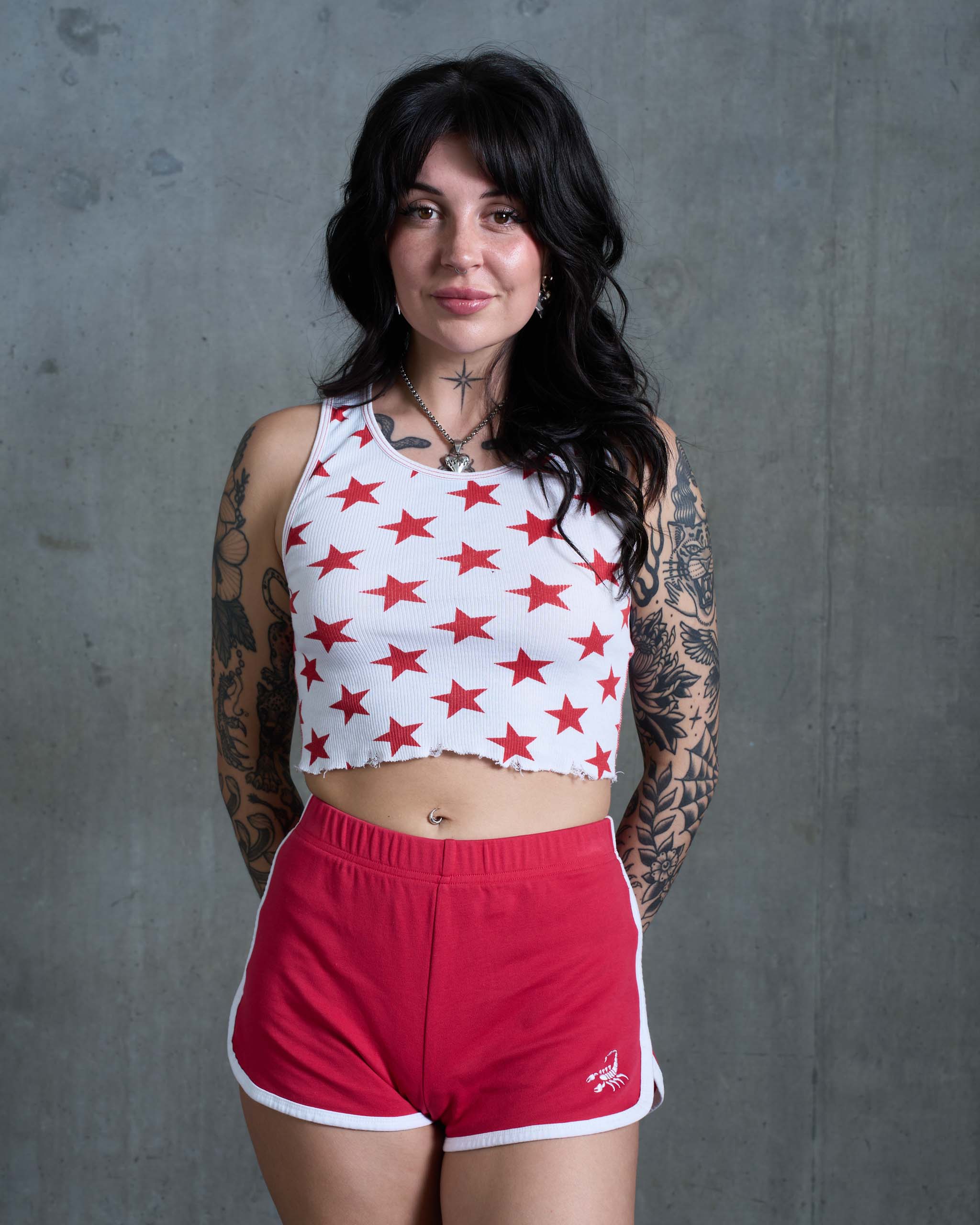A tattooed woman wearing some vintage 80's sports shorts with a star print top.