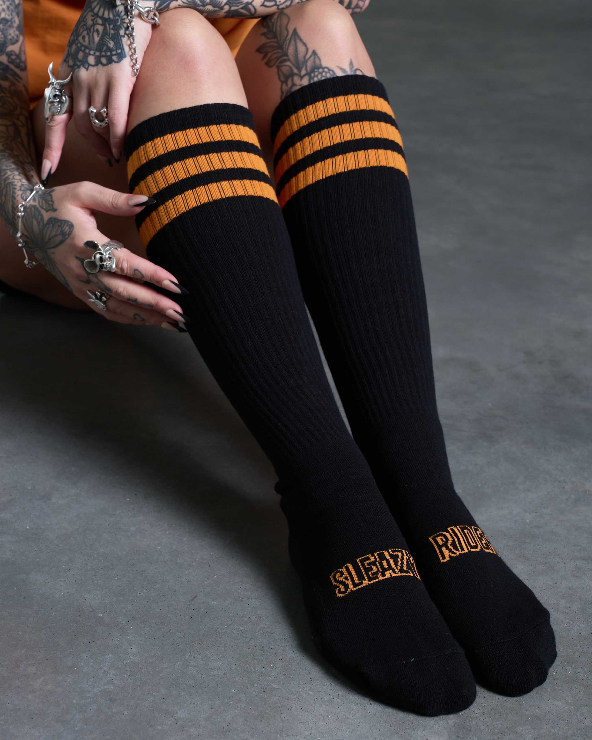 A tattooed woman sat down, wearing some Sleazy Rider black and orange socks.